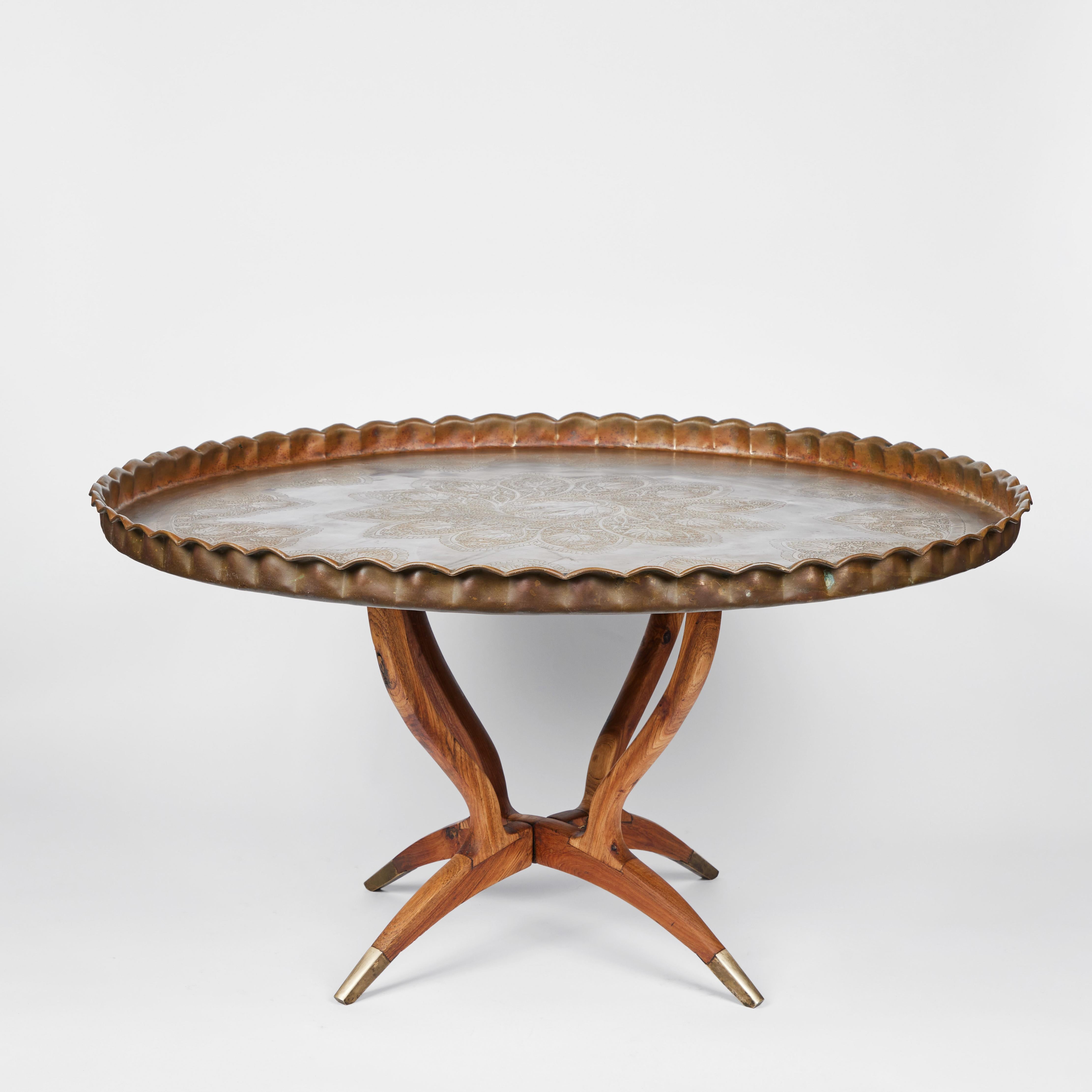 This impressive round extra large mid century brass Moroccan tray table has a lovely scalloped edge and an intricate ornamental all over design pattern on the top surface. It sits upon a rich grained folding wood base with brass feet detail on each