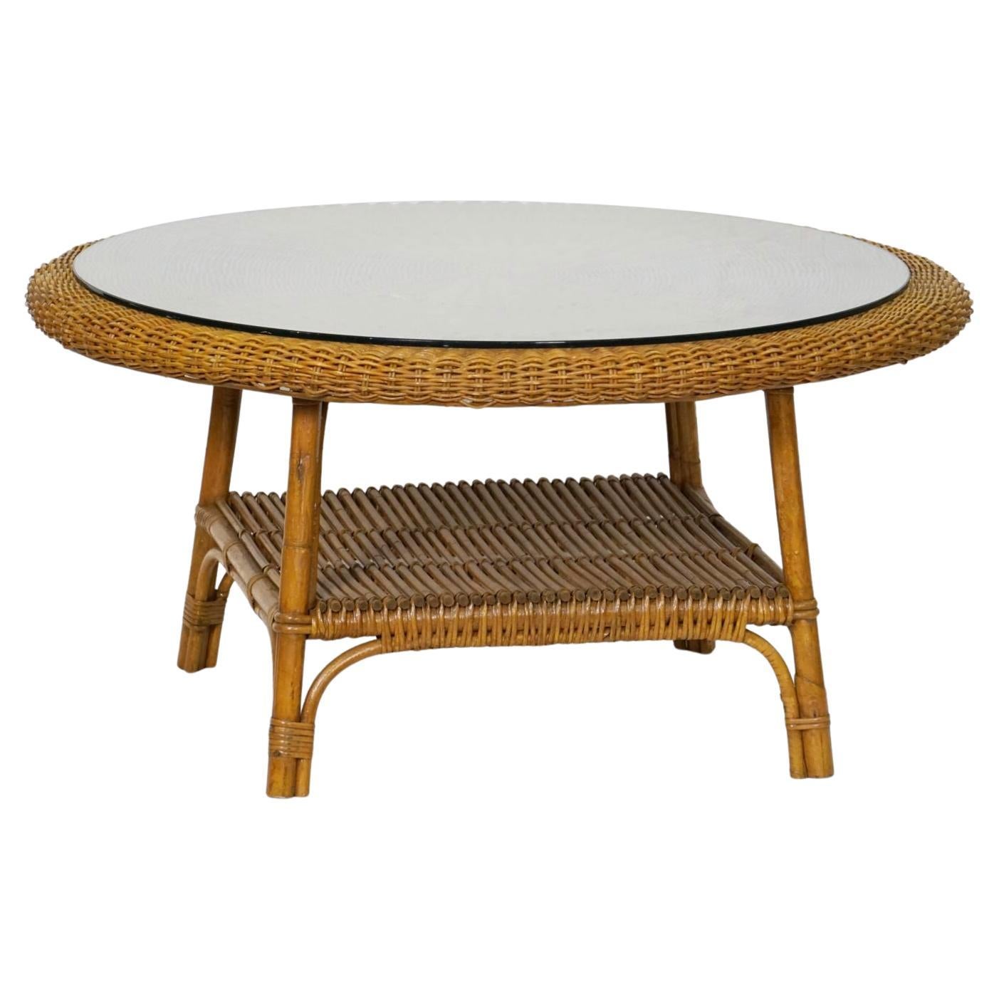 A fine midcentury round coffee or low table of woven wicker and rattan from Italy, featuring a circular top with optional round glass over a four-legged stretcher base with square under-tier shelf.