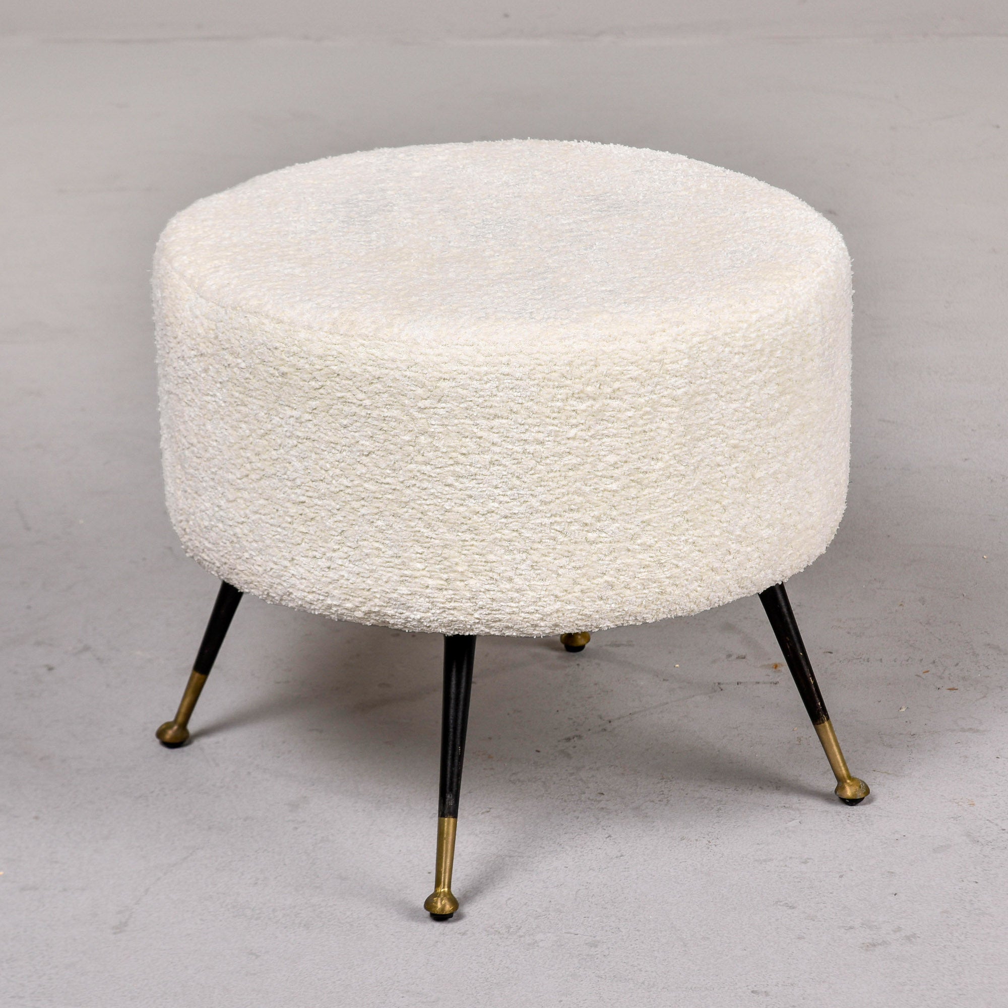 Found in Italy, this round upholstered stool dates from the 1950s. Distinct tapered black metal legs with brass-tipped feet. Newly upholstered in a creamy white, nubby textured fabric by the Italian dealer we acquired it from. Unknown maker. Two