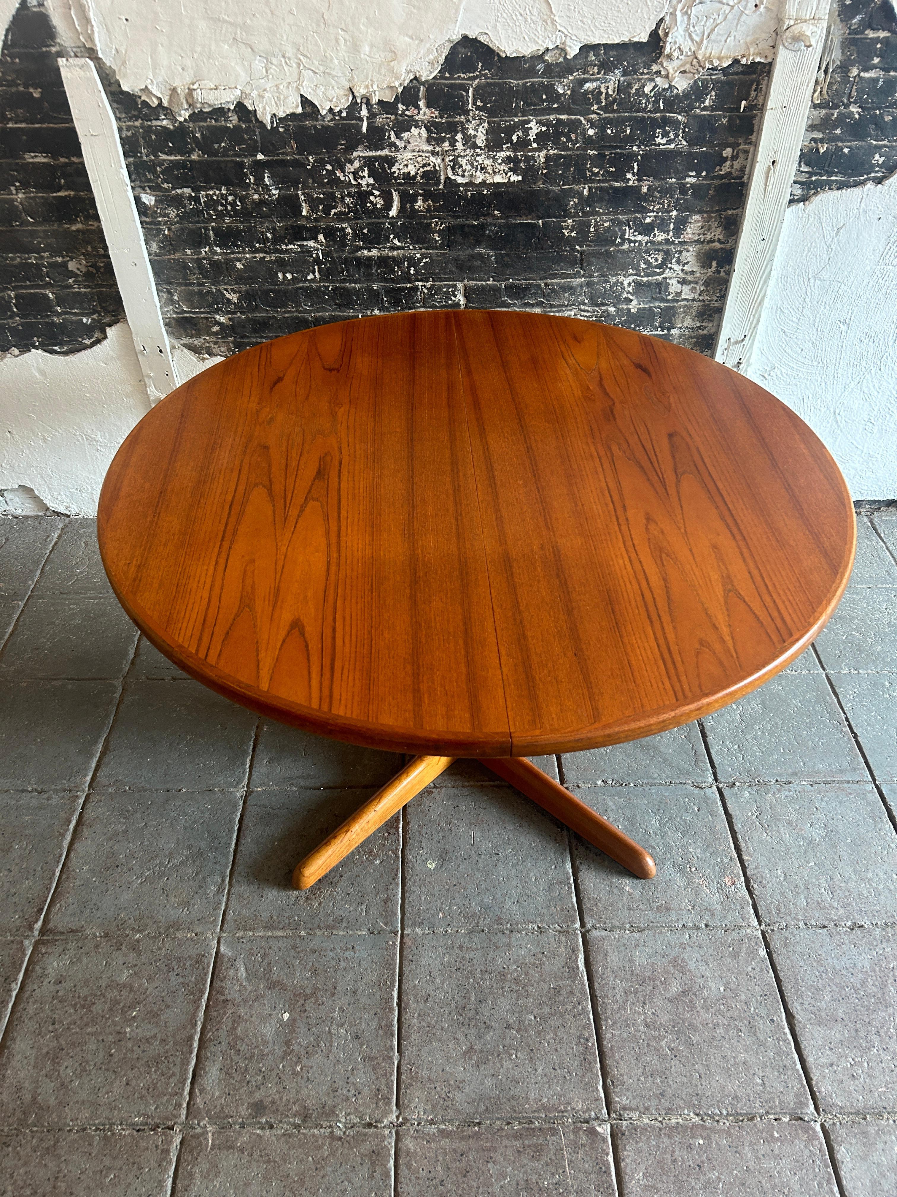 Stunning midcentury Teak Round Danish Modern extension dining table with (2) leaves. This table has beautiful Teak Veneer top with Solid Teak corners and wood legs. This table is in beautiful condition with Golden brown black teak wood tones very