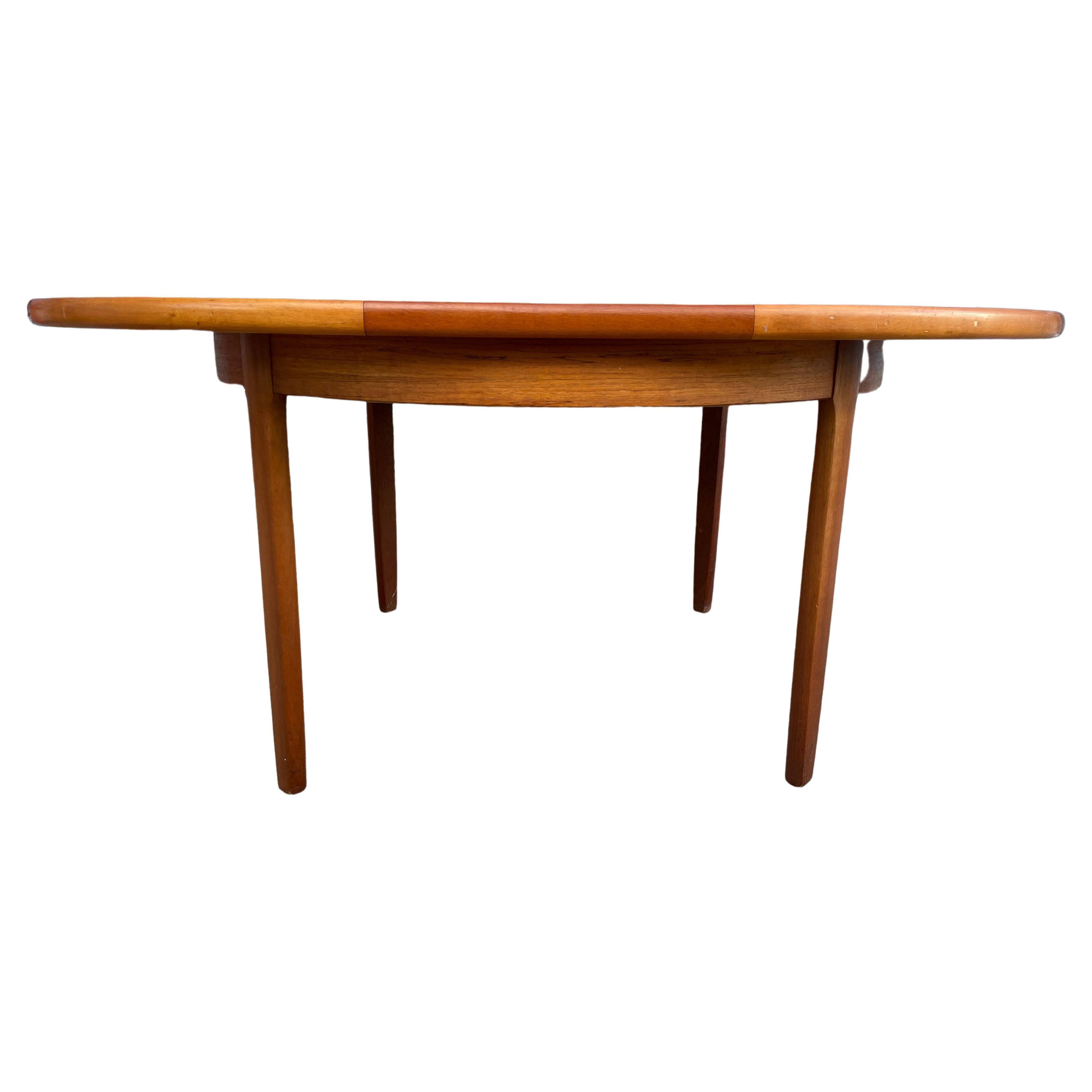 Mid century teak round Danish Modern extension dining table with 1 nesting pop up leaf. This table has solid teak legs and is in good vintage condition shows little signs of use. The leaf appears to never have been used and appears darker in color