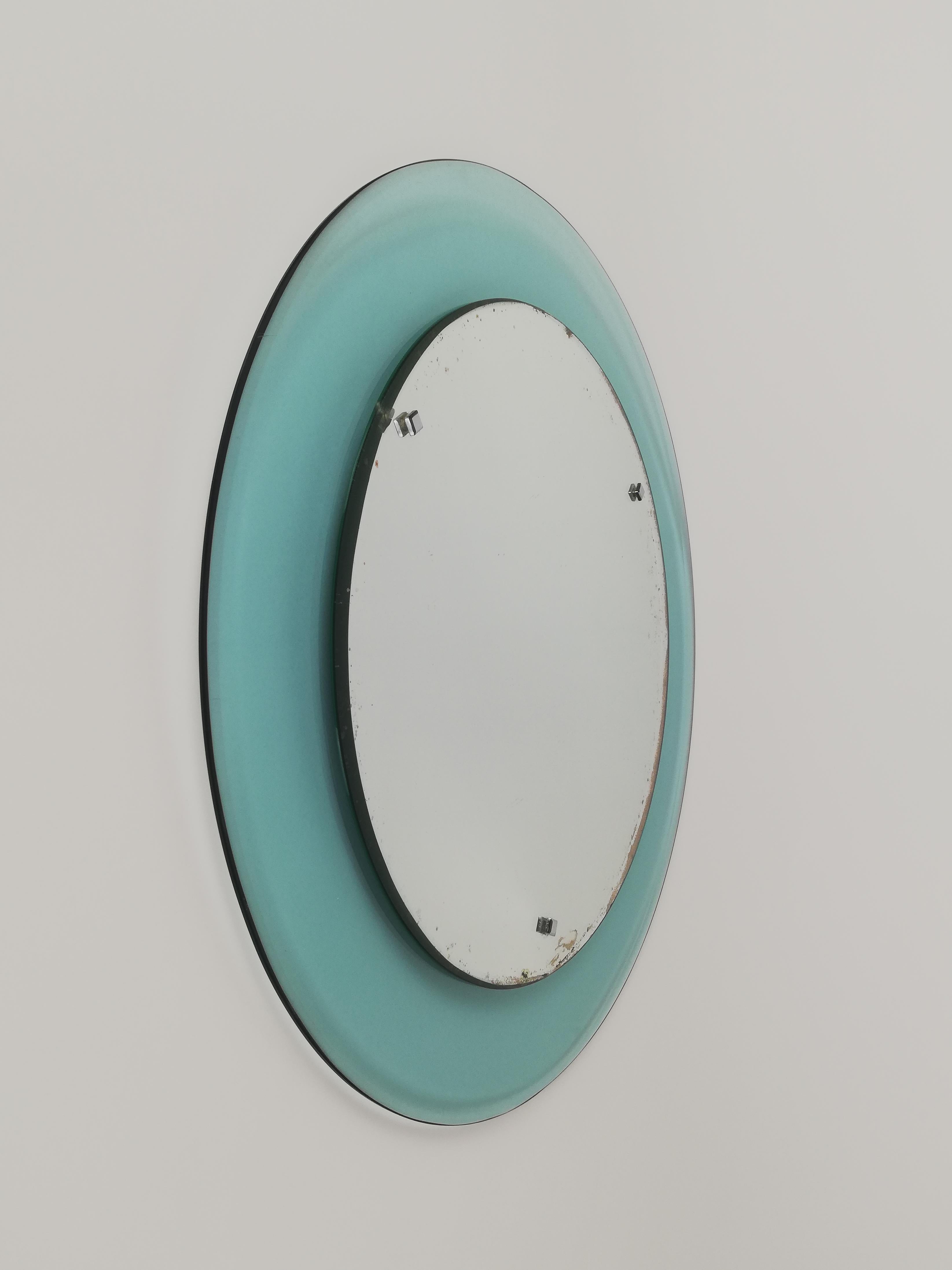 A Midcentury rounded mirror made in Italy and datable between the 1960s and 1970s.
This vintage glass mirror is attributable for materials used in manufacturing to the Veca company.
The rounded frame in turquoise transparent glass is beveled.