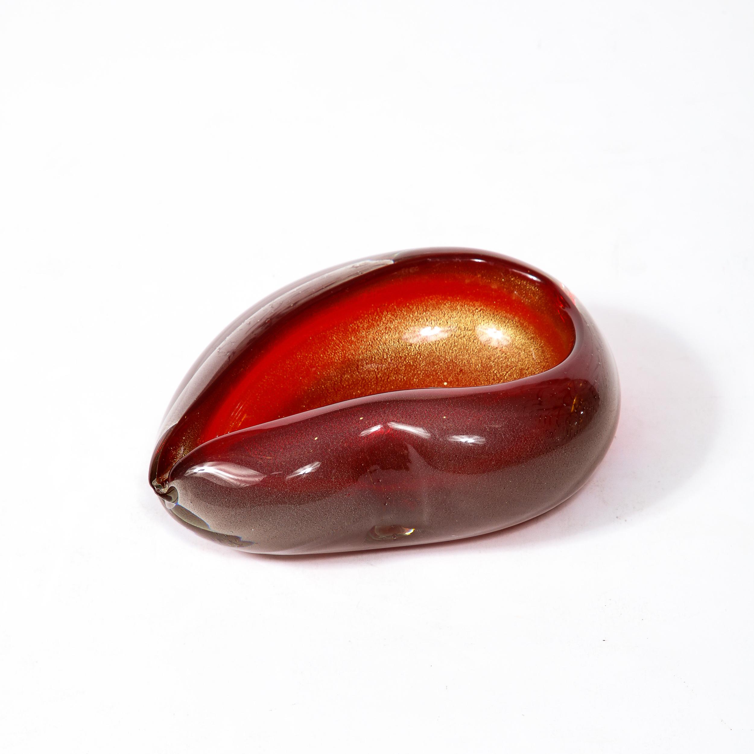 -This Mid-Century Modernist Murano Glass Dish was made in Italy, Circa 1960. Hand Blown in a deep ruby hued glass with a subtle impression and single lip detail that shape the piece, the sunken basin contains glittering 24Karat Gold Flakes.