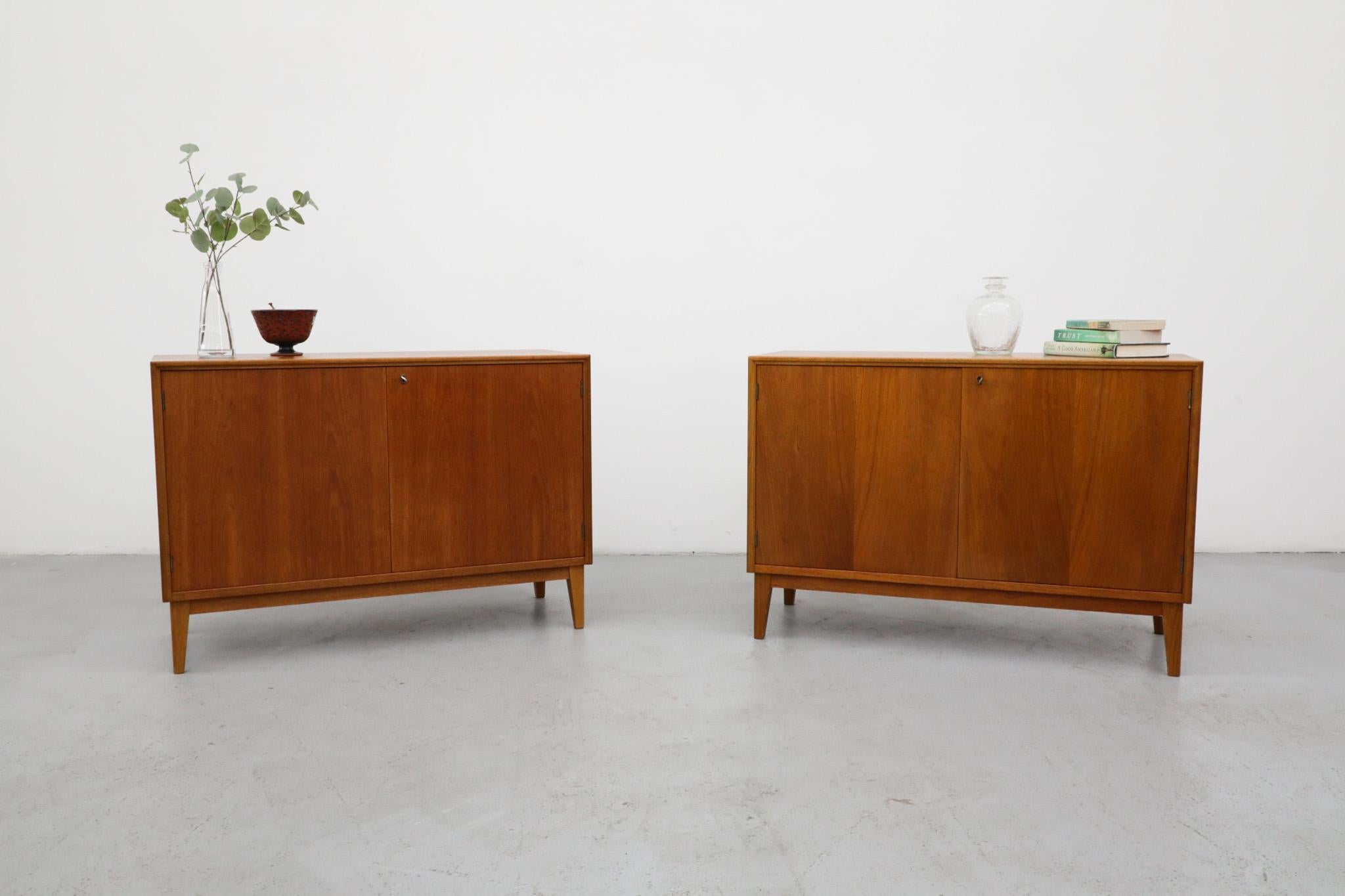 Mid-Century locking double door teak storage cabinets with shelves. Lovely wood grain with angled teak legs. In original condition with some visible wear and fading consistent with regular use. Comes with a key. Two available, sold individually.