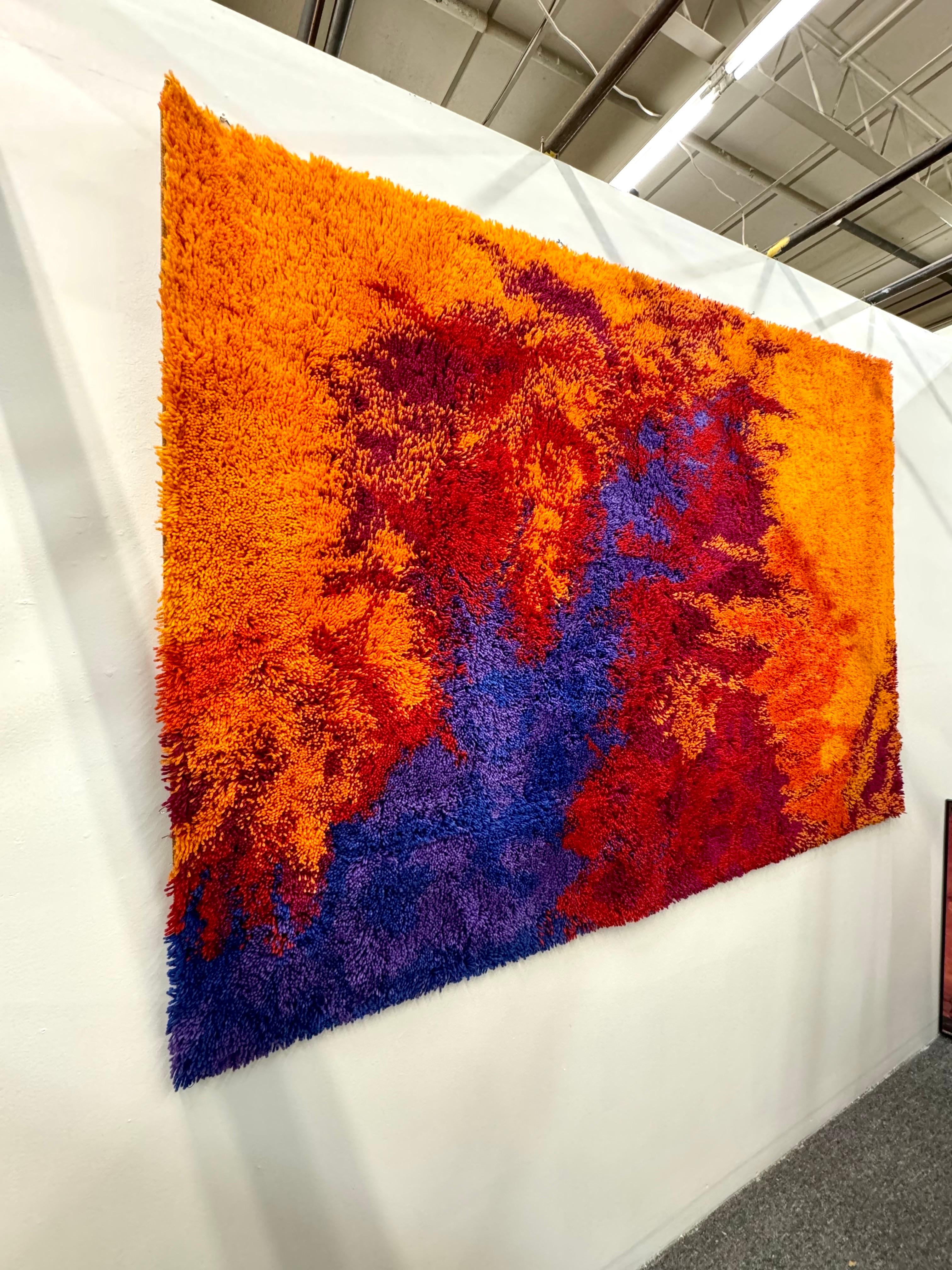 A vintage Danish area wool rug made by Rya in Denmark circa 1960s. The bright colored rug features long shaggy fibers and remains in excellent condition. On the background of mottled red colors in subtle different shades, splashes of purple and