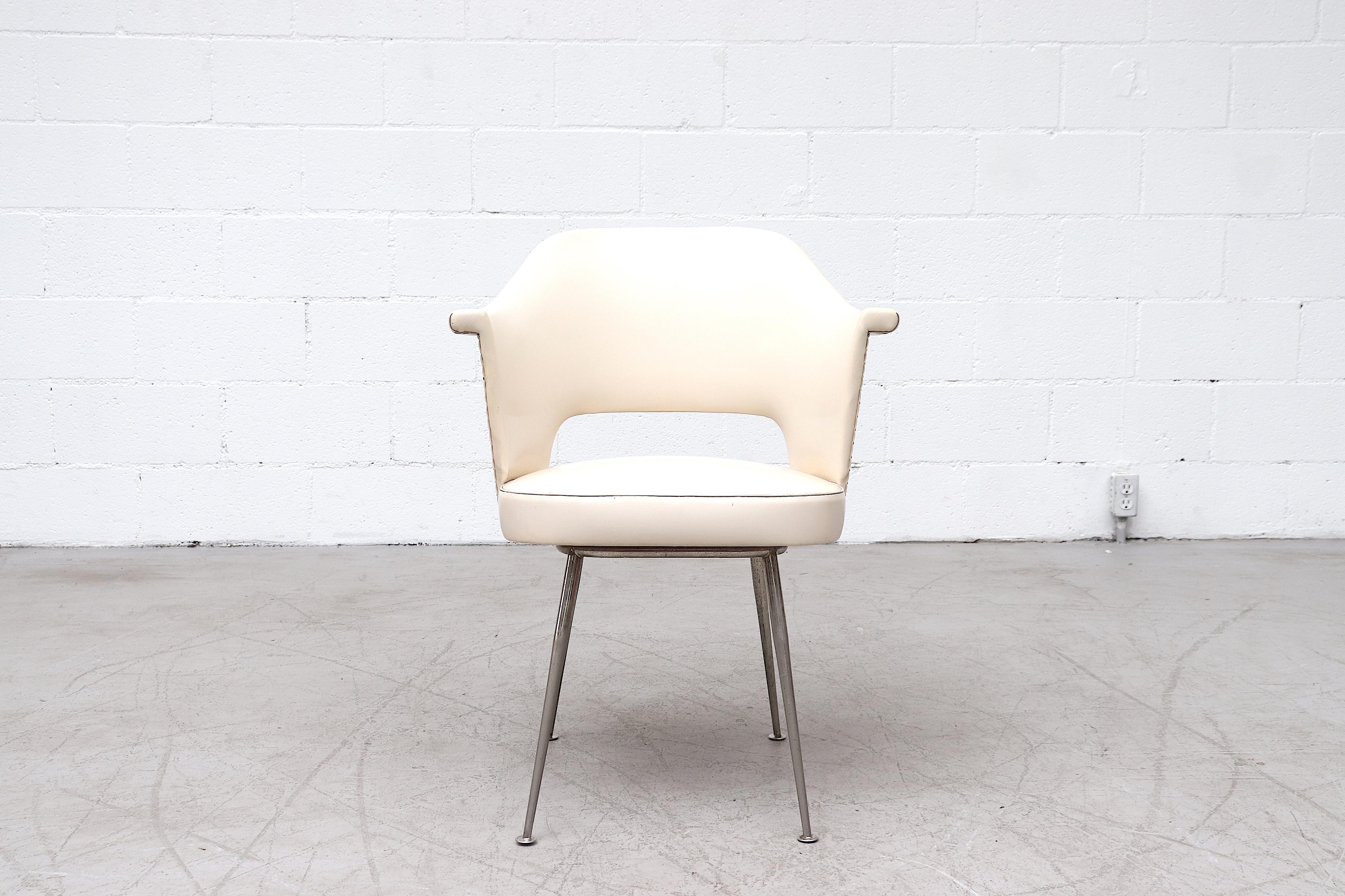 Stunning Saarinen style arm chair with white Skai upholstery and tapered metal legs. Stunning design with smooth lines and stud accents. In original condition with visible wear, including some discoloration and heavy patina to the metal legs. Wear