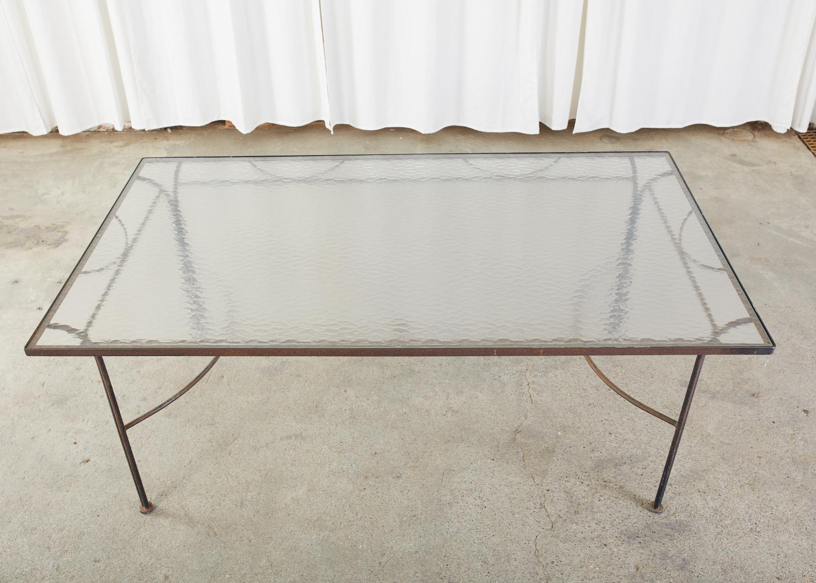 Mid-Century Modern wrought iron garden patio dining table in the manner and style of John Salterini. The table has a large frame crafted from round iron poles supporting a rectangular top inset with a frosted pane of glass. Each corner leg has two