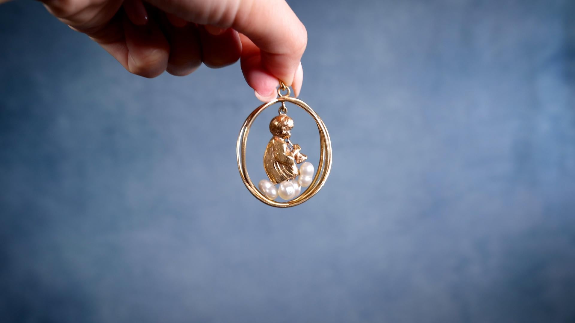 One Mid-Century Sapphire and Pearl Cherub 14k Yellow Gold Pendant. Featuring two round cut sapphires with a total weight of approximately 0.05 carat and three baroque pearls. Crafted in 14 karat yellow gold, weighing 23.72 grams. Circa 1960. The