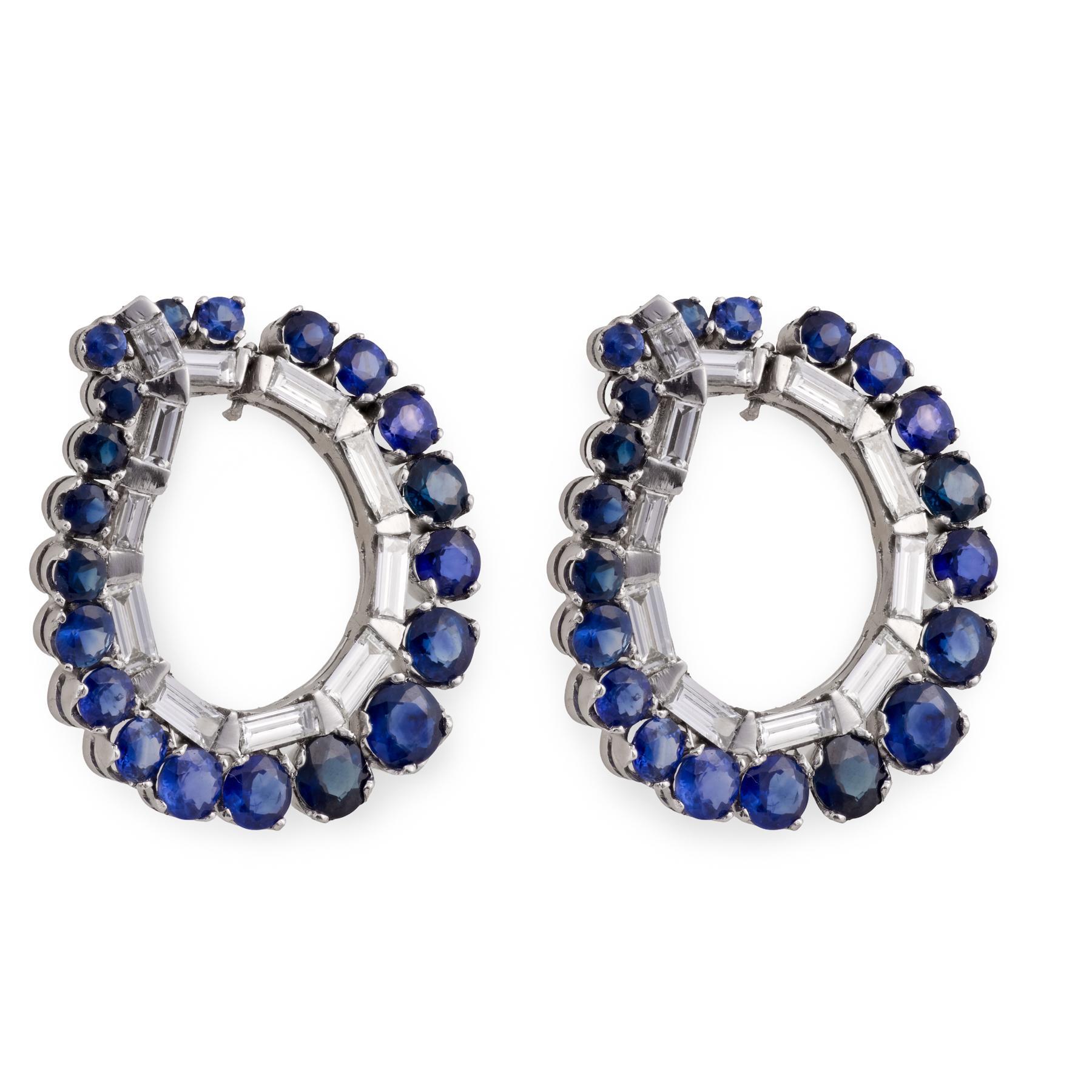 Radiosi e architettonici, questi orecchini a cerchio in platino della metà del secolo scorso presentano una vivida serie di quaranta zaffiri blu il cui ricco colore risplende con una profondità accattivante. Tra gli zaffiri, ventidue diamanti taglio