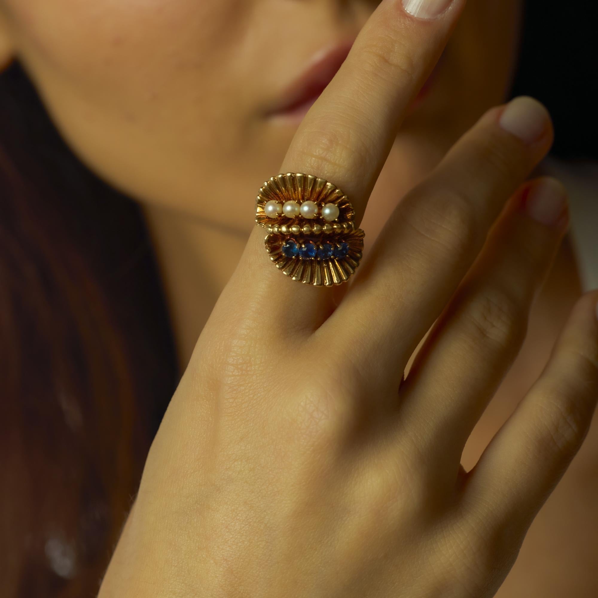 Este anillo único de mediados de siglo, de 1956, equilibra elegancia y color con cuatro zafiros azules redondos de talla brillante que suman aproximadamente 0,80 quilates, emparejados con cuatro perlas luminosas de unos 3,74 mm cada una. El rico