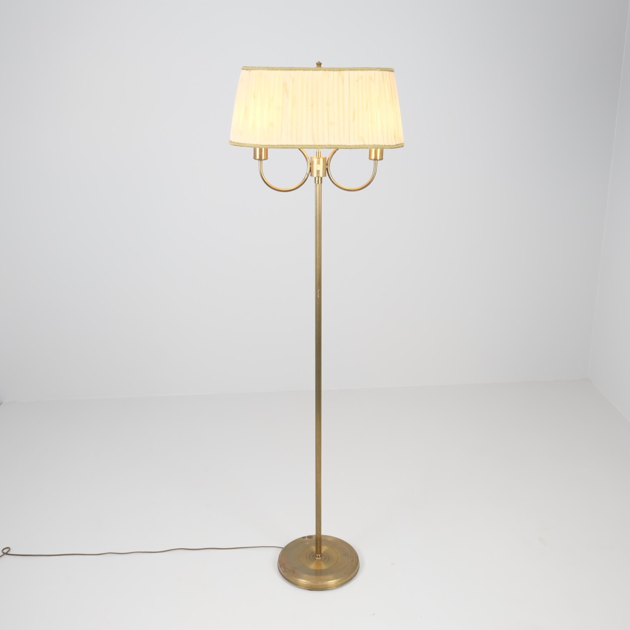 Elegante lampada da terra della metà del secolo scorso, probabilmente di origine scandinava, forse finlandese o svedese, realizzata in ottone con una patina calda e invecchiata. Il design è caratterizzato da uno stelo sottile e minimalista che si