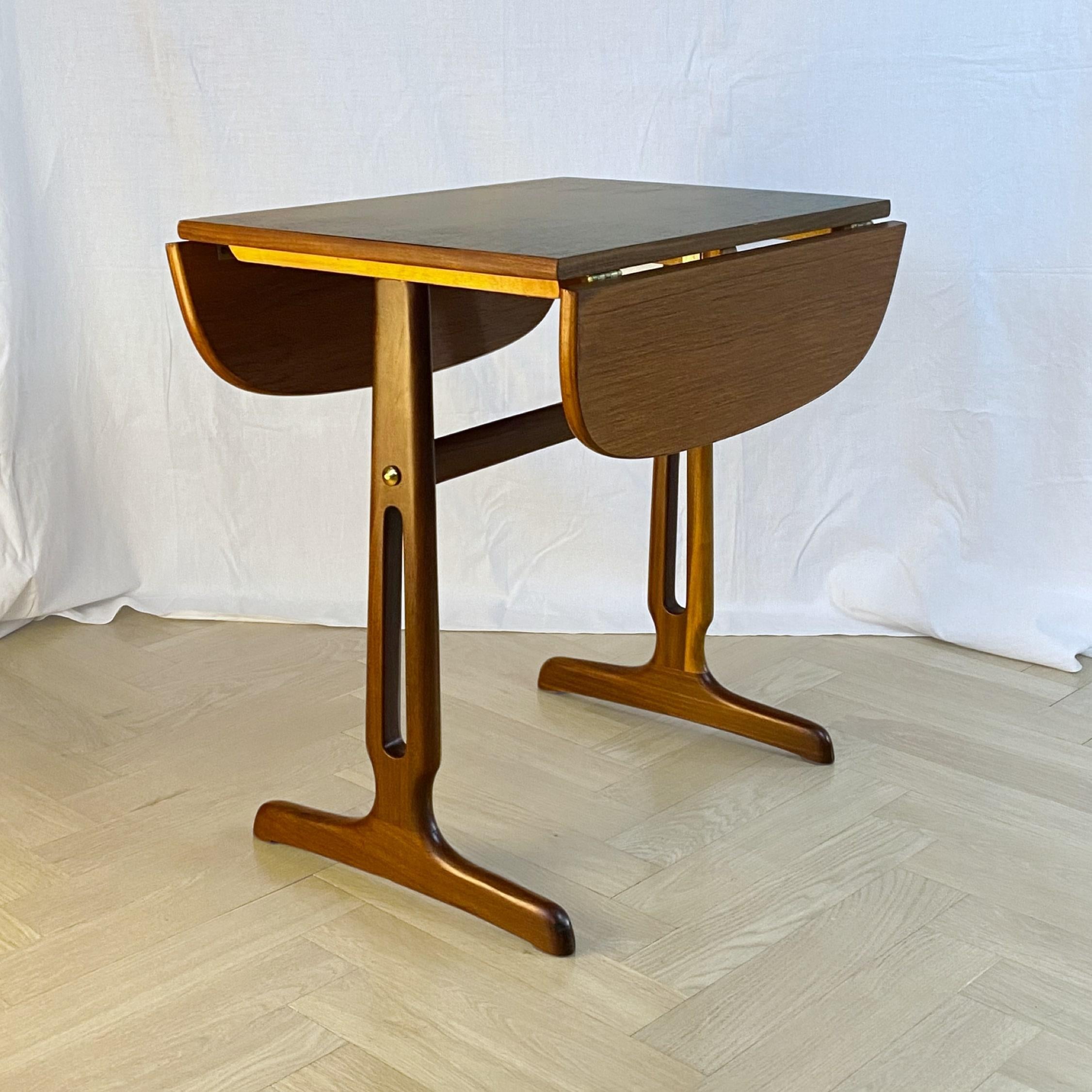 A neat drop-leaf side table or coffee table, made from solid teak and teak veneer with brass fittings. Slightly oval table top with black centerpiece resting on decorative legs. Produced by an unidentified Swedish manufacturer in the 1950s. Height