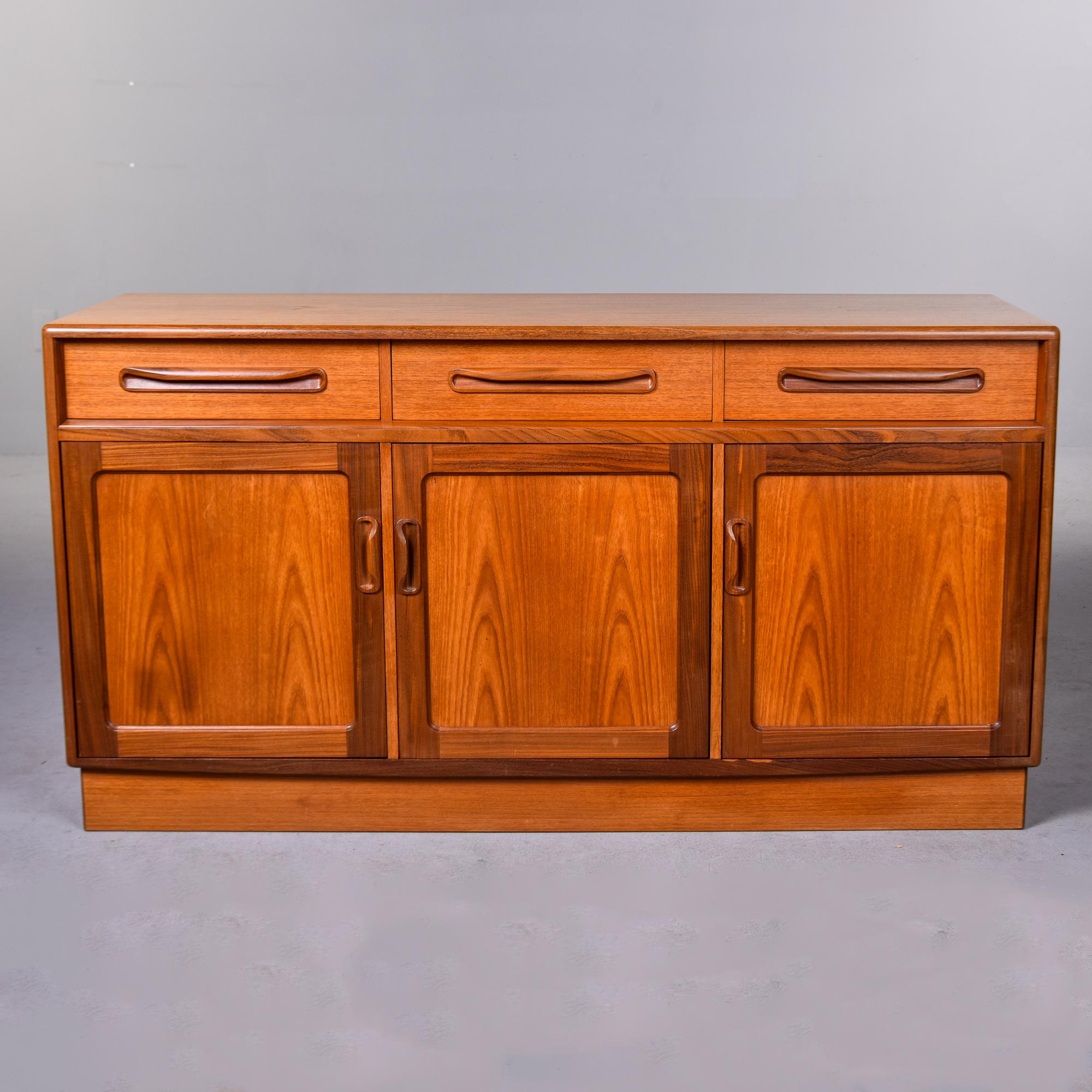 circa 1960s medium sized buffet in teak by British maker G Plan. Three narrow top drawers with integrated pulls in darker, contrasting wood over three open storage cabinets with hinged doors and single internal shelves. Contrasting darker trim on