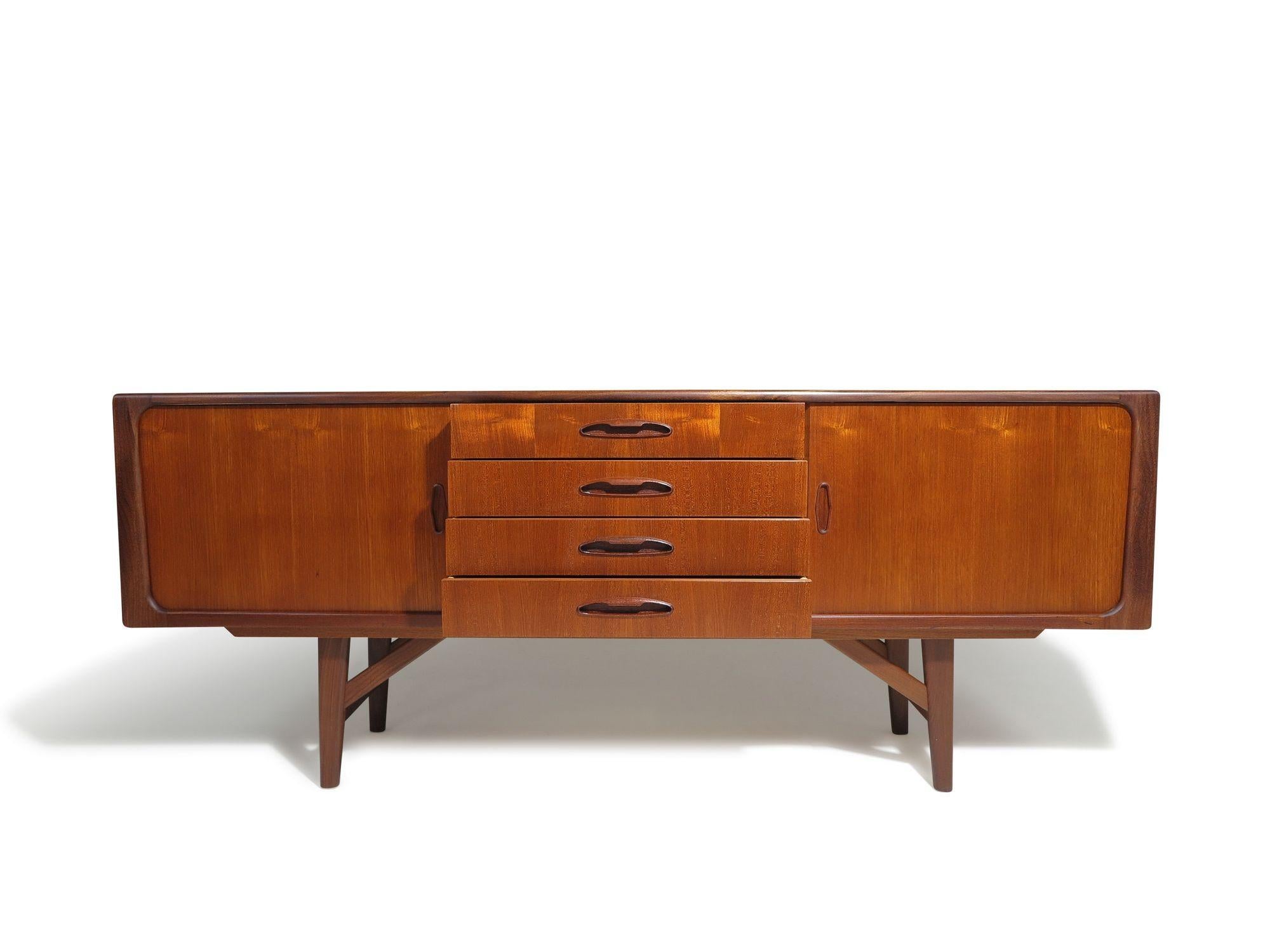 Handcrafted from beautifully grained old-growth teak, this mid-century Danish low credenza features two sliding doors that open to reveal a mahogany interior with adjustable shelves. The center section offers a series of four drawers, each lined in