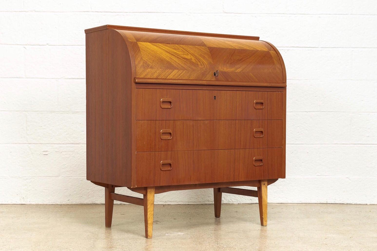 This iconic mid century Swedish modern Egon Ostergaard teak cylinder rolltop secretary desk cabinet is circa 1970. The classic Scandinavian modern design has clean minimalist lines and features a beautiful inlaid diamond-patterned rolltop surface.