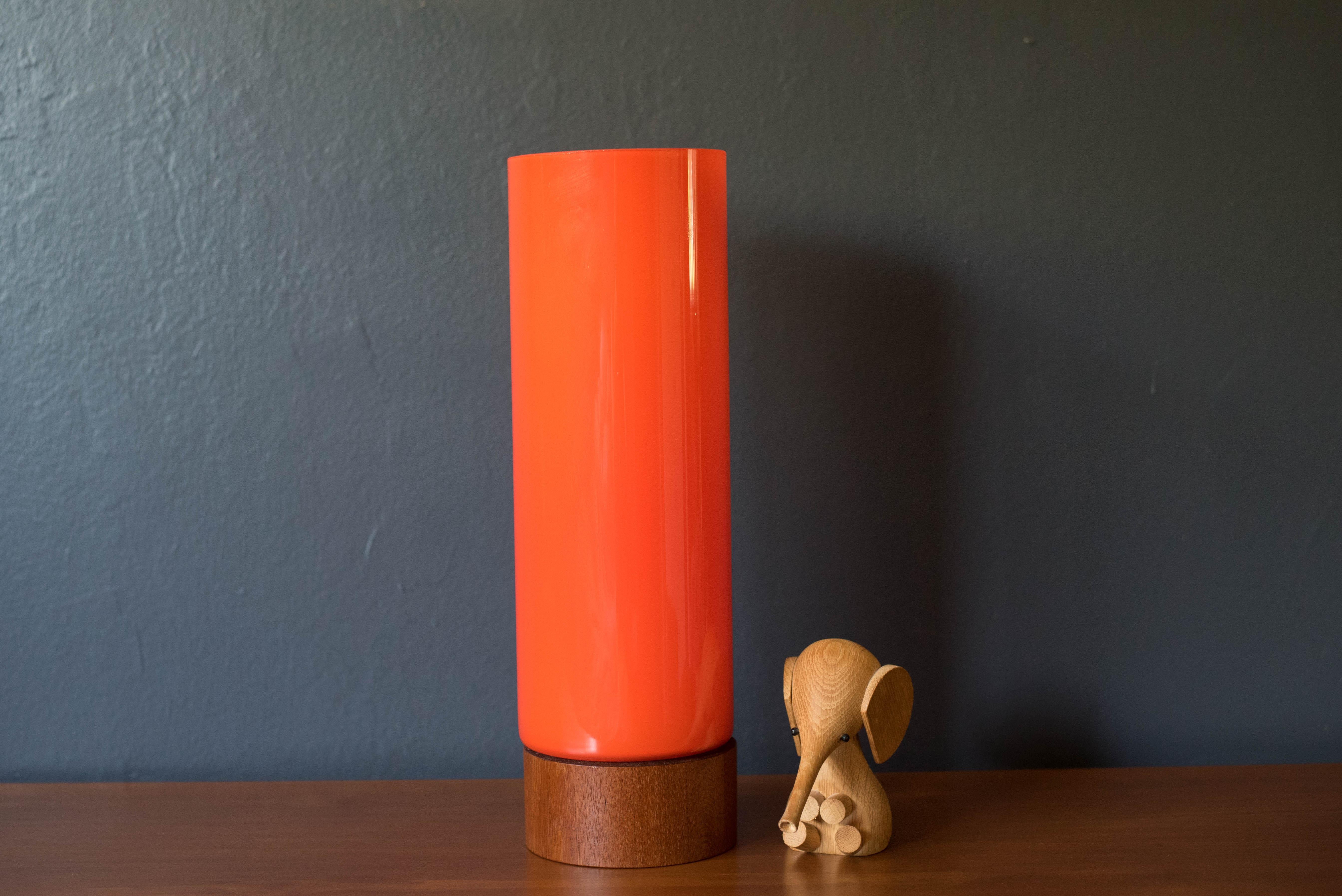 Vintage Scandinavian modern accent table lamp circa 1960s. This piece is encased with a vibrant orange cylinder hand blown glass shade accented with a white frosted interior and a supporting teak base.