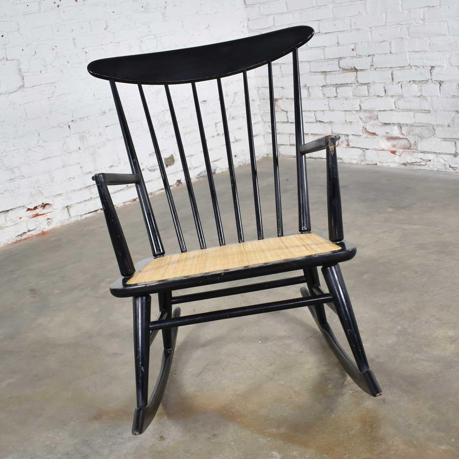 Handsome black painted midcentury spindle back rocking chair in a Scandinavian Modern or Danish modern style with a natural cane seat. This rocker is in wonderful vintage condition. The original painted finish has a nice age patina which includes