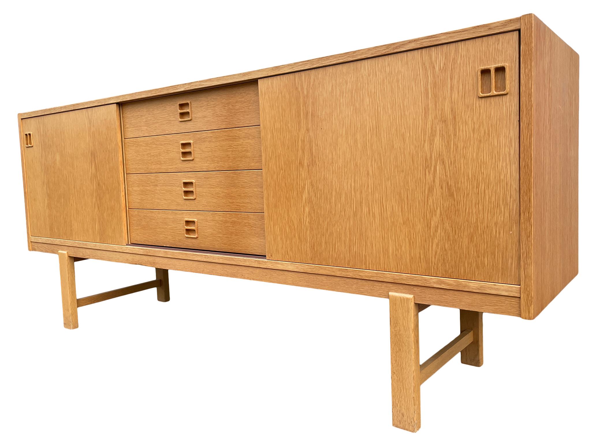 Mid-Century Scandinavian Modern teak low 4 drawer credenza with 2 sliding cabinet doors with an adjustable shelf in each cabinet. Beautiful designed low dresser or credenza - blonde teak wood veneer with sculpted handles. Sits high on a pair of