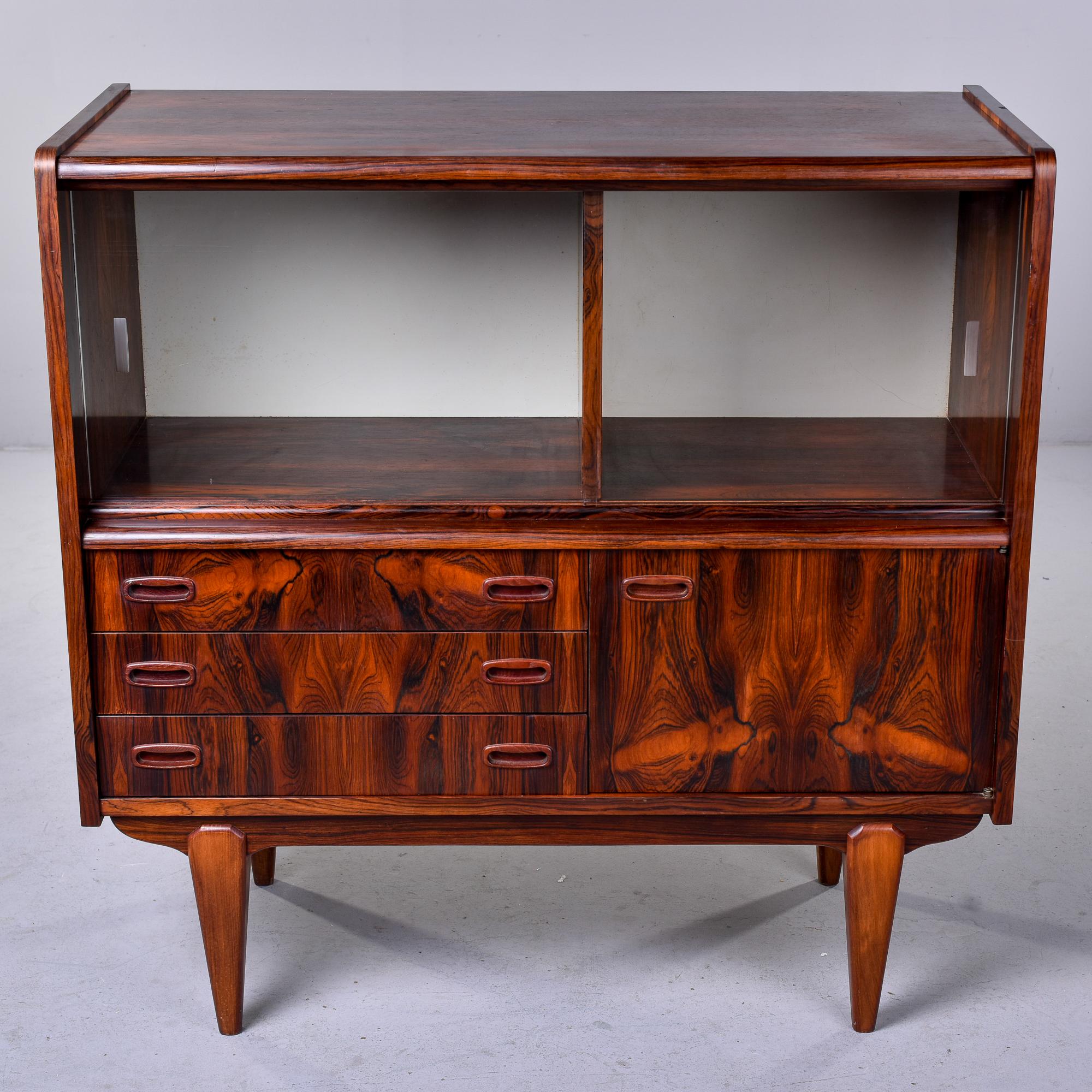 Circa 1970 Scandinavian bar cabinet in dramatically figured rosewood veneer features two sliding glass doors on the top section over three felt lined drawers on one side and a storage compartment with internal shelf on the other. Tapered legs.