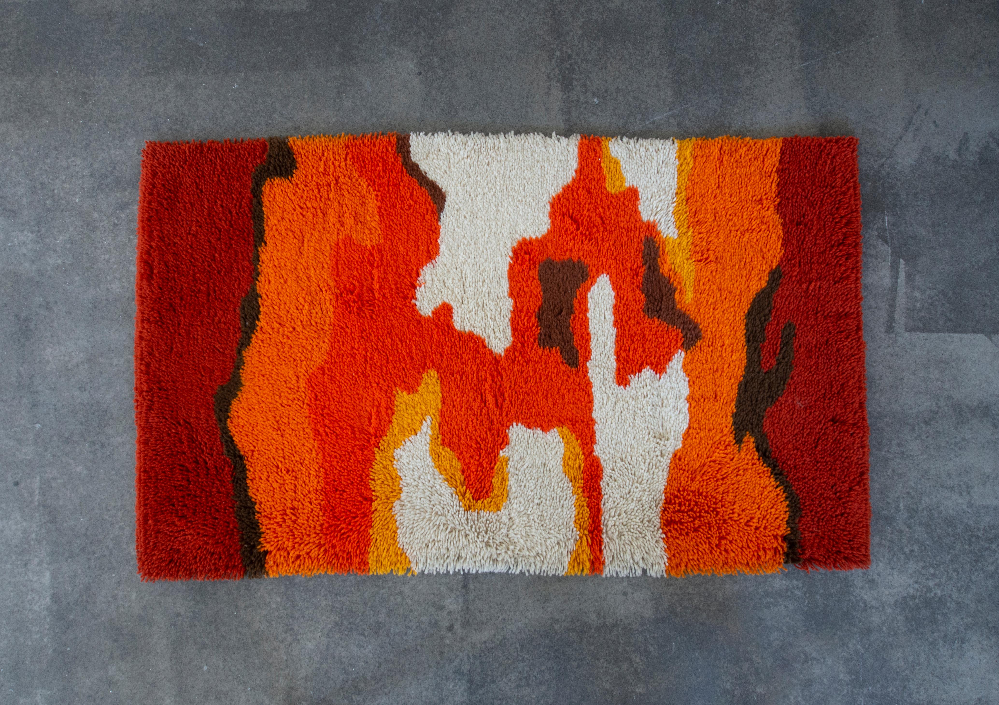In this listing you will find a beautiful, vibrant Rya Rug in yellow, orange, red, brown and white. It features long threads, creating a fluffy feeling bellow your feet. There is an organic flow of the colors, creating a warm and welcoming feeling