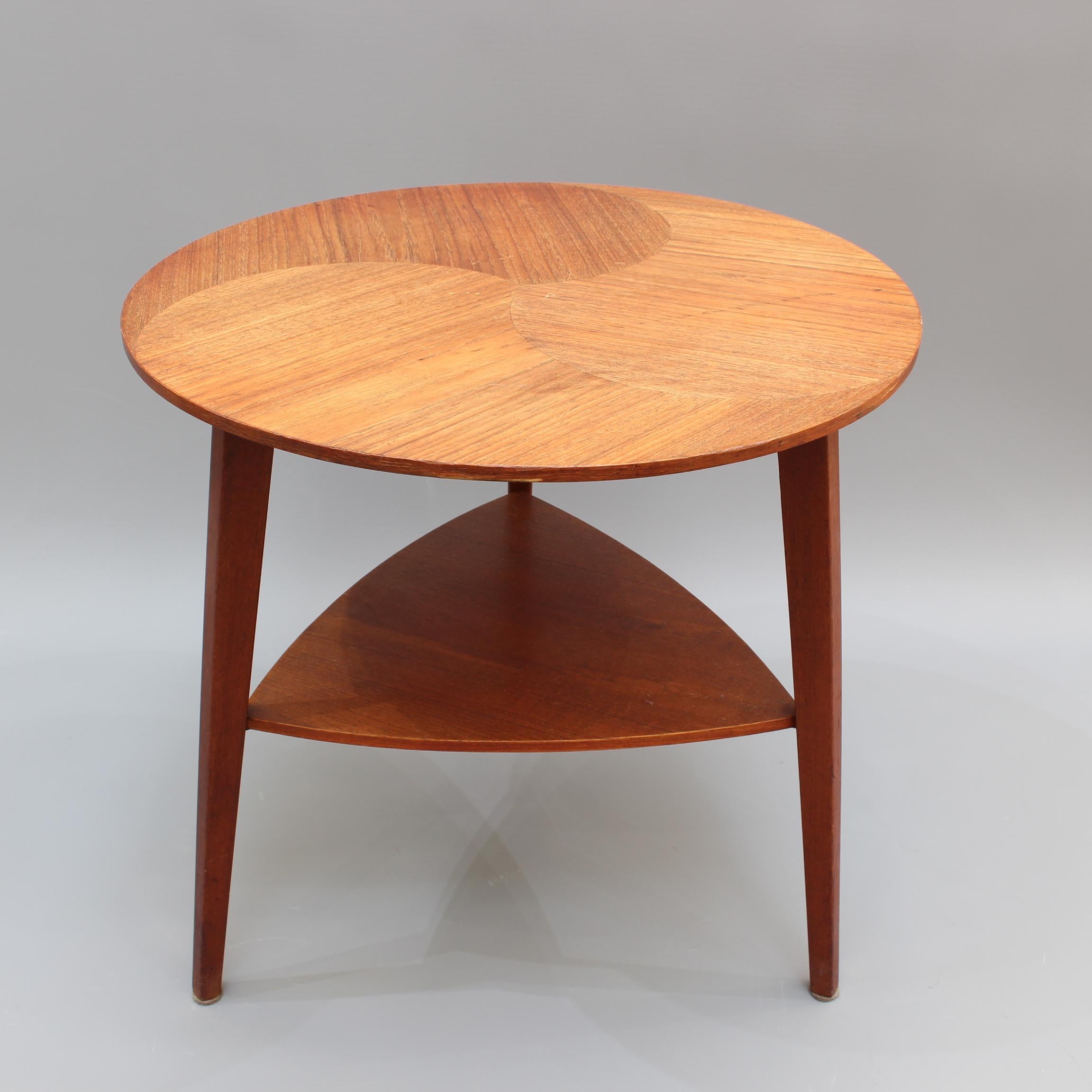 Midcentury Scandinavian side table (circa 1960s). A characterful side table with wood veneer, circular top and triangular-shaped lower storage surface structured with tripod legs. Quintessential midcentury Scandinavian design all in one piece.