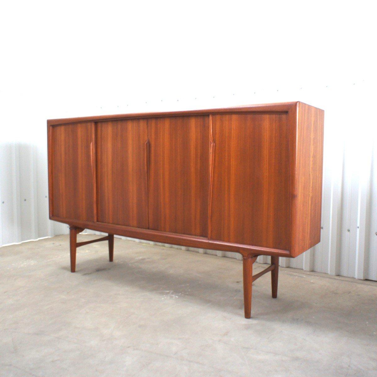 Rare and sculptural scandinavian sideborad by Axel Christensen for ACO Mobler, from the end of the 1950's. The footing has a slight compass shape. It has four sliding doors. with each handles carfeully designed. Each door reveales teak shelves and
