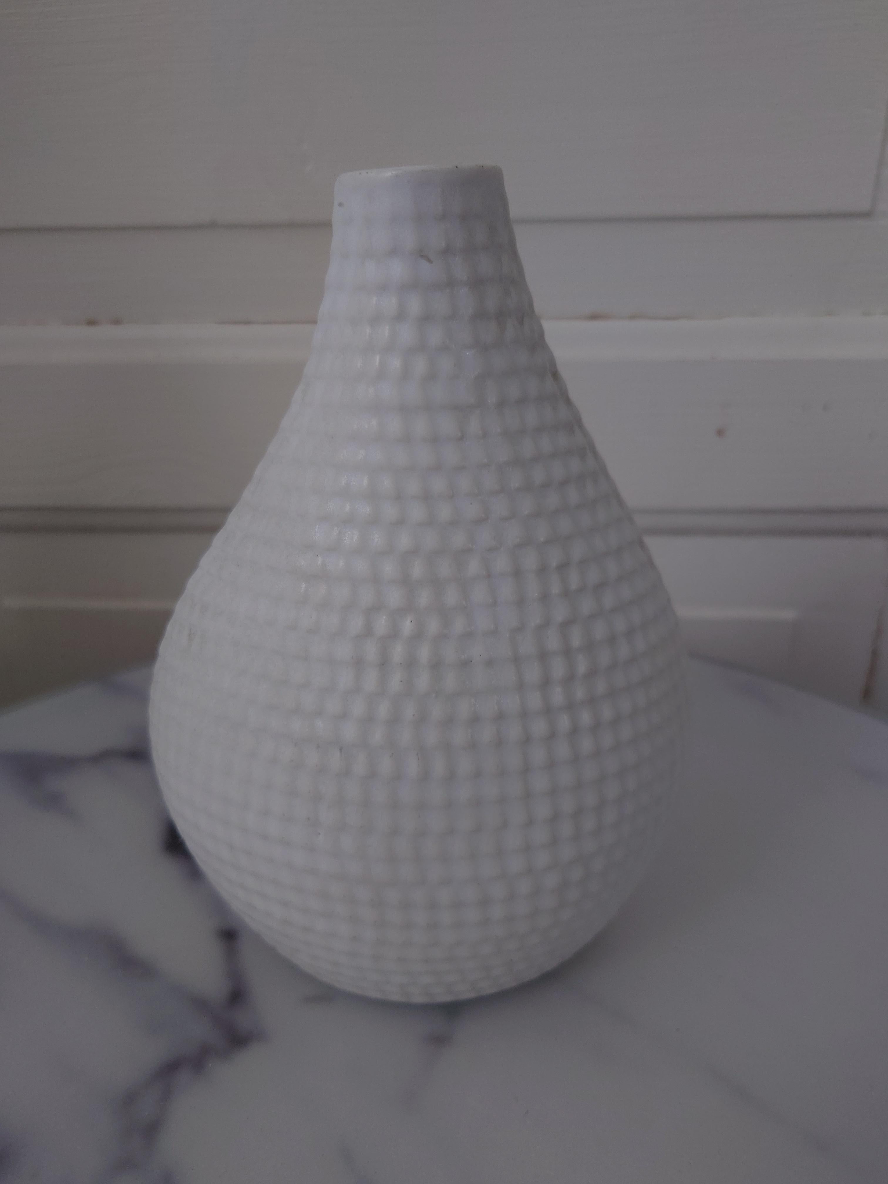 Vaso in ceramica bianca opaca Stig Lindberg per Gustavsberg Reptil. Conserva le etichette originali sul fondo.
Il vaso Reptil di Stig Lindberg è un design sorprendente con una superficie unica che ricorda la pelle dei rettili. È caratterizzato da