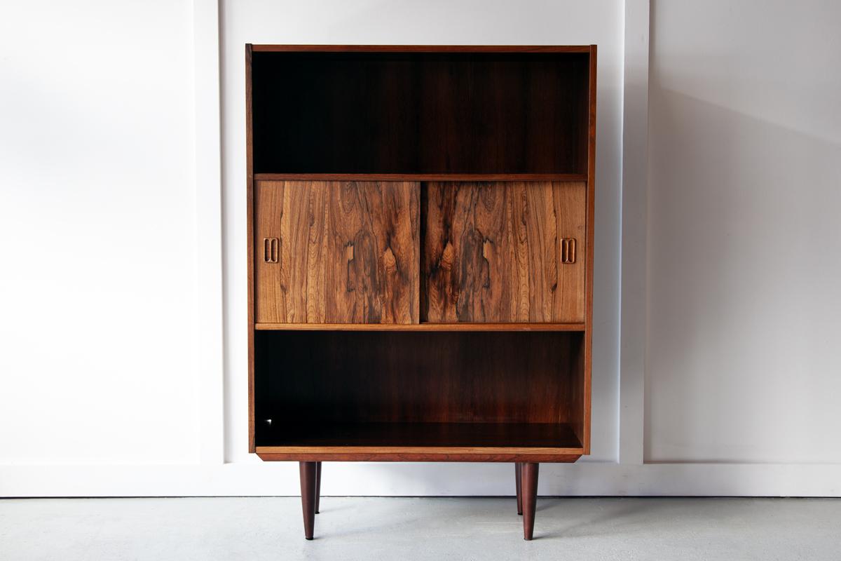 An ideally sized storage unit in beautifully grained rosewood with two open shelves and a central closed compartment with siding doors. This lovely unit features classic mid century detailing in the inset handles and a elegant tapering legs. 