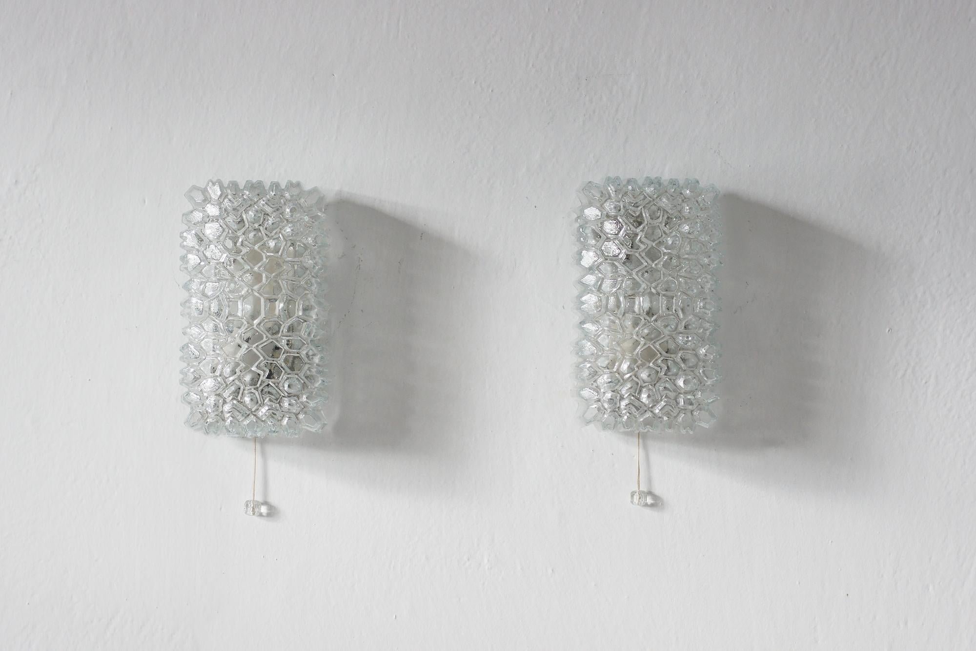 A set of two wall lamps manufactured by the renowned German manufacturer Glashütte Limburg, known for its perfect craftsmanship and modernist forms.

The lampshades are made of colorless glass with a distinctive geometric texture that beautifully
