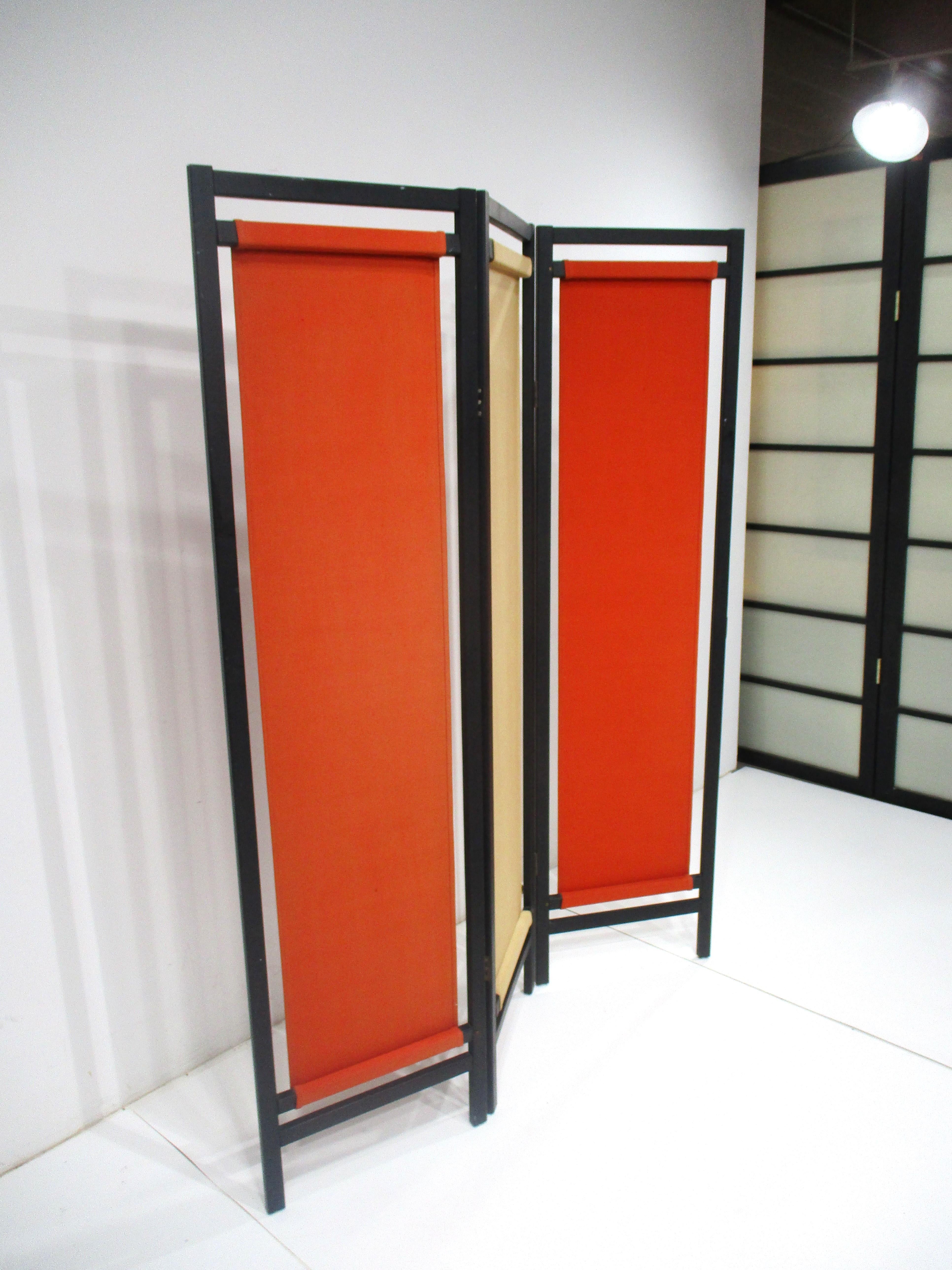 A colorful three panel folding screen with canvas inserts in burnt orange and tan . The screen is highlighted by a satin black wood frame which would give a room that extra detail and punch of rich color . Manufactured by the Gold Metal Folding