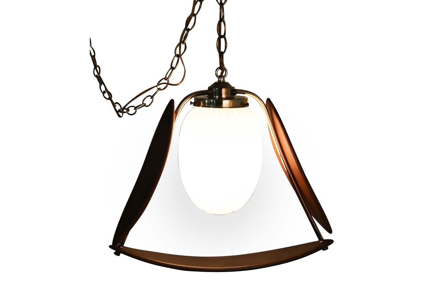 A sophisticated, interesting Mid-Century Modern pendant light, swag lamp, chandelier featuring a milky white glass globe with a raised ribbing that follows the billowing egg shaped globe. The globe is framed in a triangular form by three gorgeous