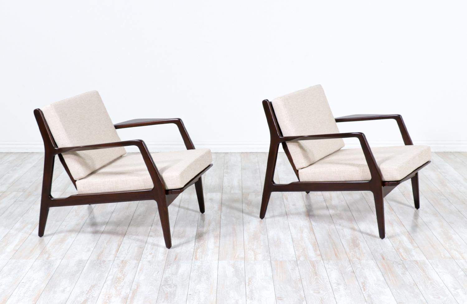 Pair of stylish lounge chair designed by Ib Kofod-Larsen for Selig in Denmark circa 1960s. These sleeks and ergonomic lounge chairs features a sturdy walnut-stained beech-wood frame with angled legs and a sculptural slatted back that is held in