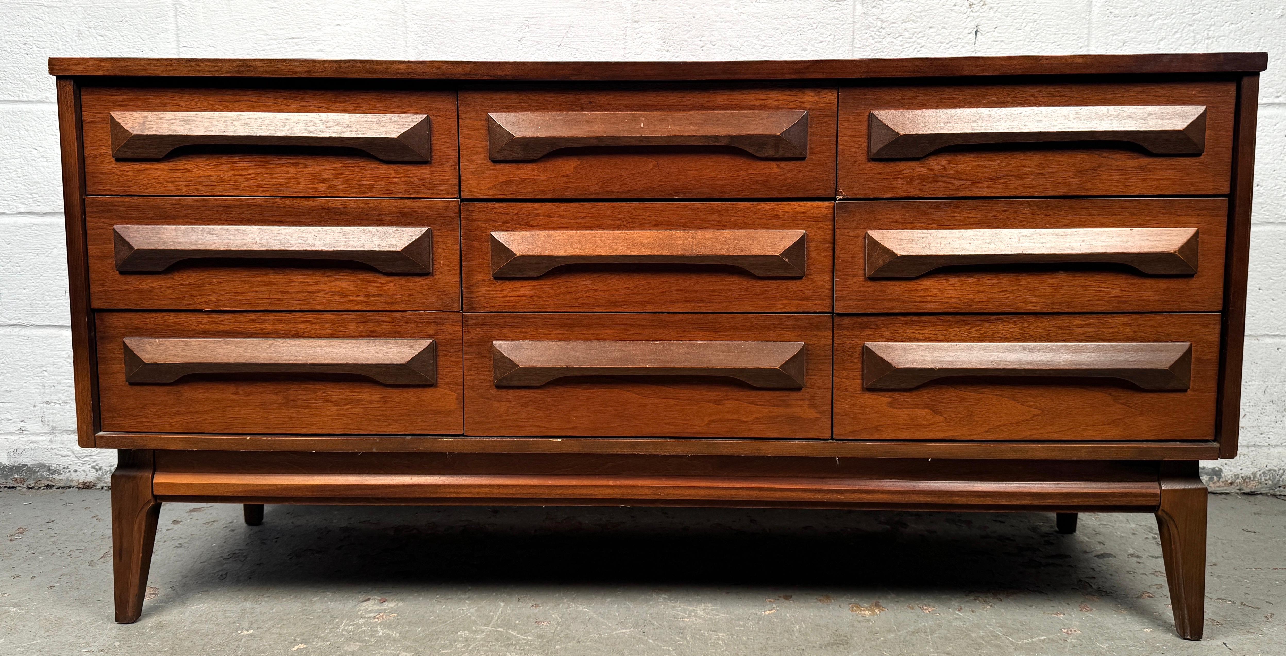 Bring vintage sophistication into your home with this Mid-Century Sculpted Nine Drawer Dresser, a statement piece that combines sleek lines with bold design. Featuring dramatic sculpted drawer fronts and a warm wood finish, this dresser captures the