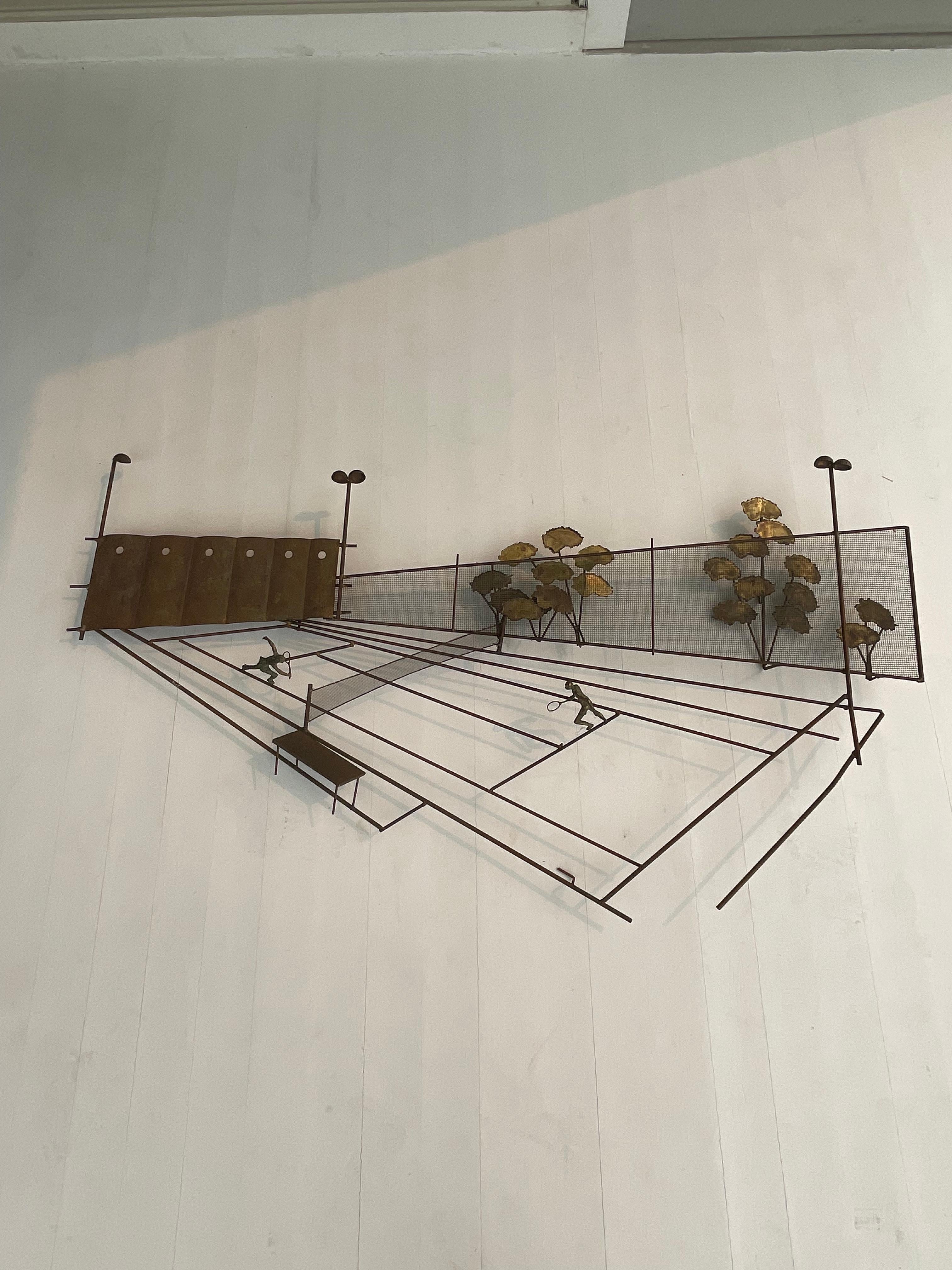 Mixed metal sculpture of a tennis match is signed by C.Jere. It features two players holding rackets playing with a metal net in a stadium with flowers on the outside fence . Curtis Jere is known for eccentric design and often displays playfulness
