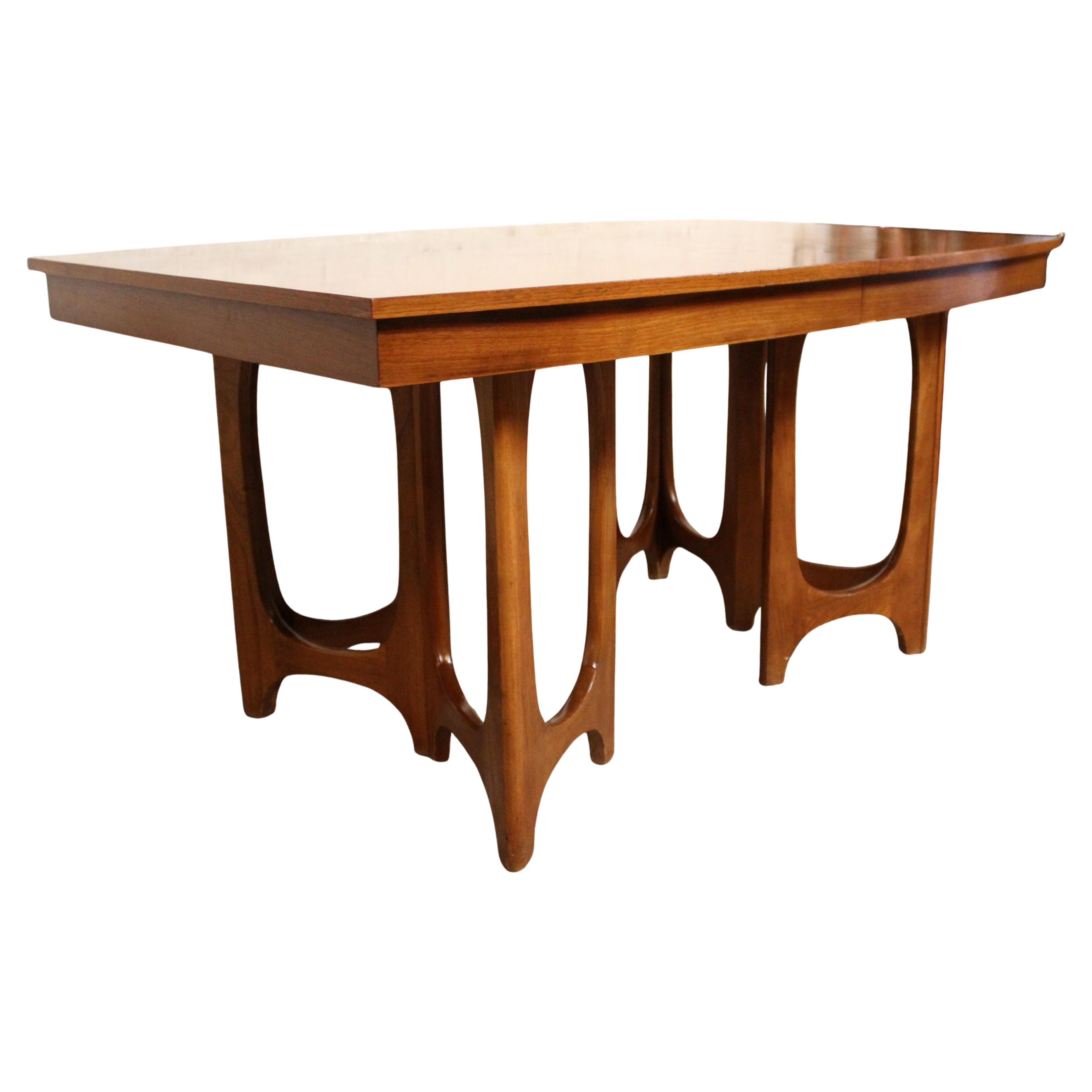 A stunning Mid-Century dining table crafted by Young Manufacturing Co., this piece is a beautiful example of American modernism. The table features a warm walnut finish and a sculptural double pedestal base with arched cutouts, showcasing the