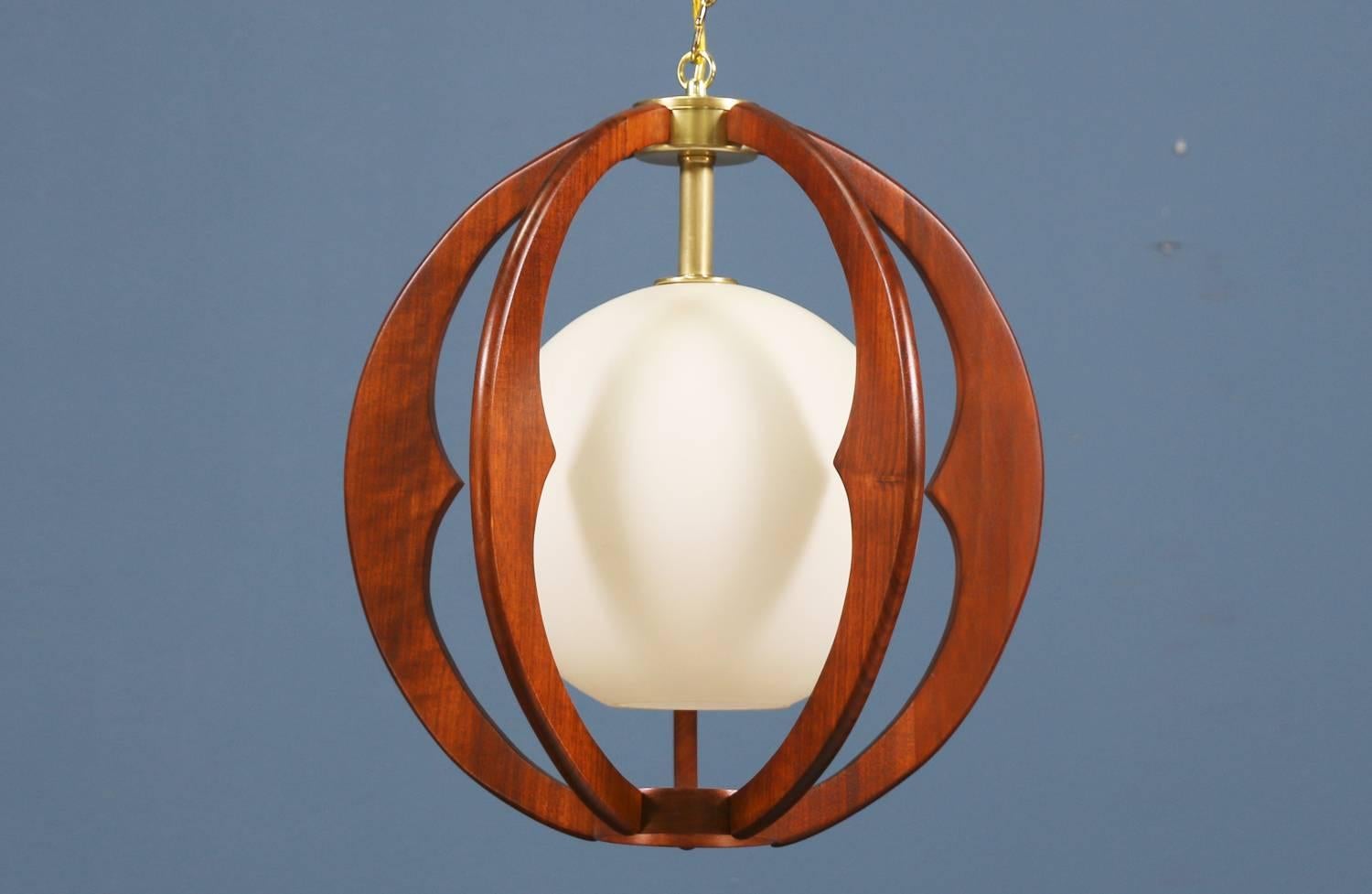 Modern globe pendant chandelier designed and manufactured in the United States, circa 1960. This delicate chandelier features a white glass shade enclosed in a spherical walnut wood frame with brass accents. This beautiful design is subtle yet