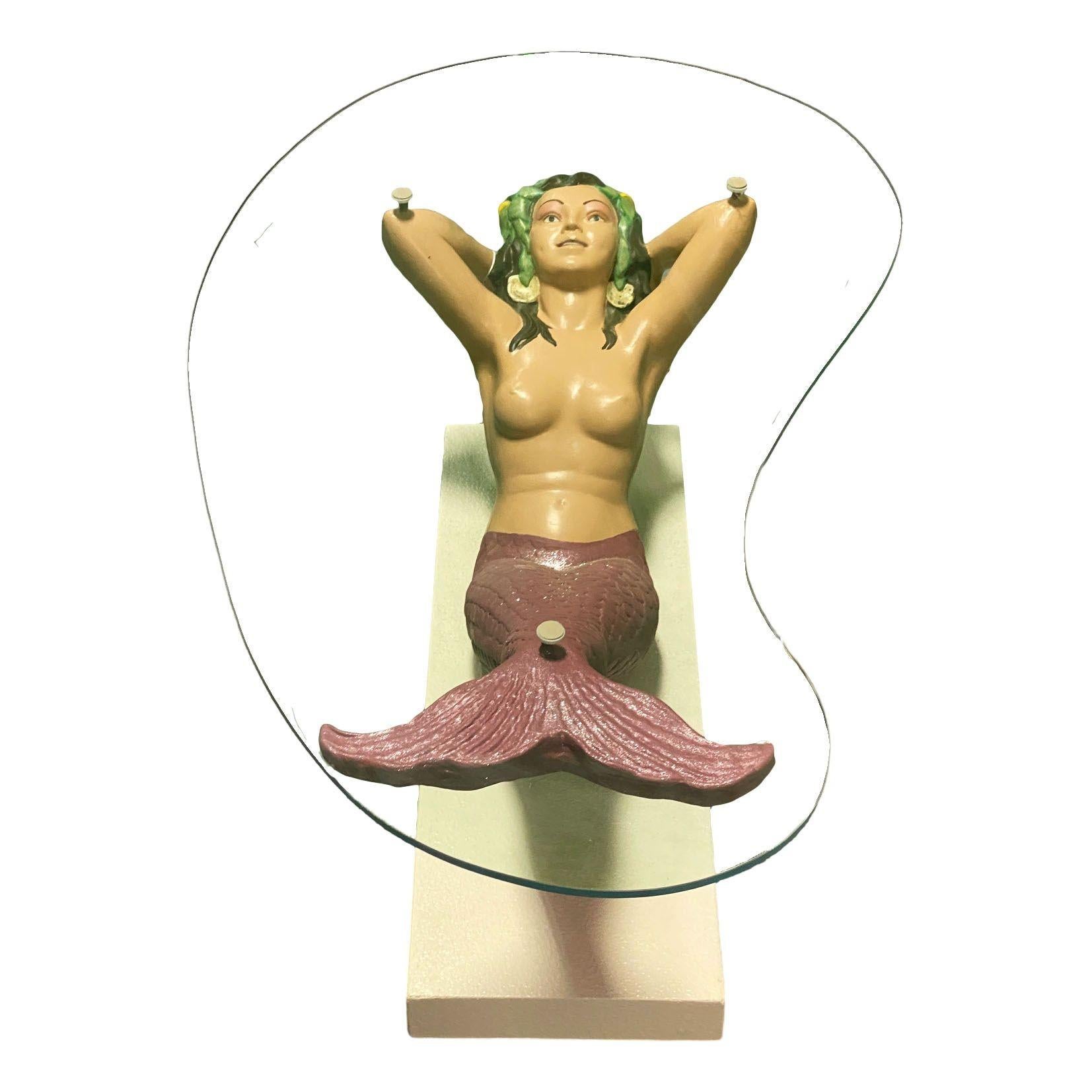 Rare table à café/cocktail entièrement restaurée avec une base sculpturale en composite représentant une impressionnante sirène de près de 2 mètres de long. La figure semble flotter gracieusement vers la surface, soutenant un plateau de verre