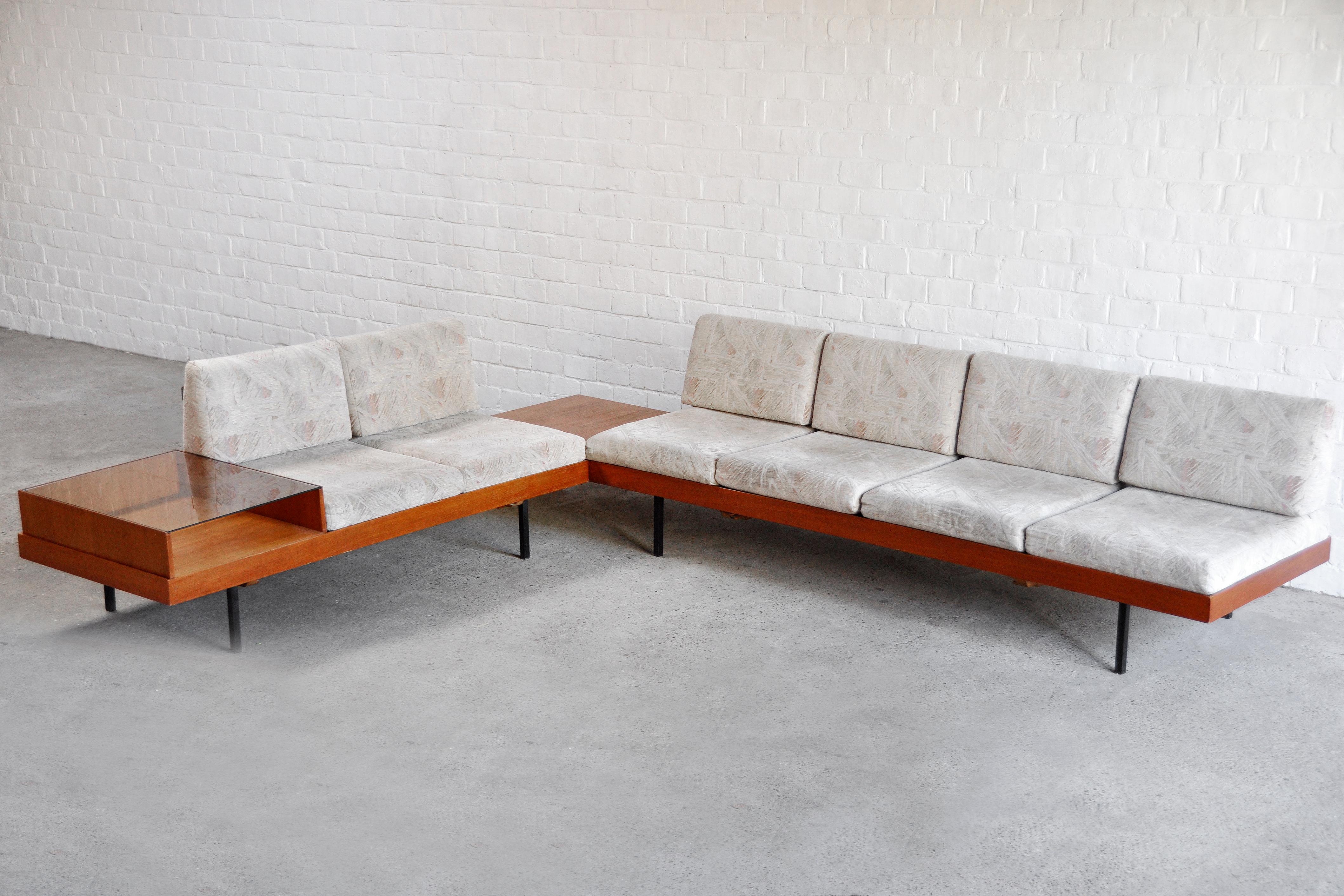 A large mid-century corner sofa with wooden side tables/display cabinet produced in Germany in the 1960s. This sectional corner sofa consists of four modules with a frame in warm glazed teak and loose seat and back cushions. The cushions are