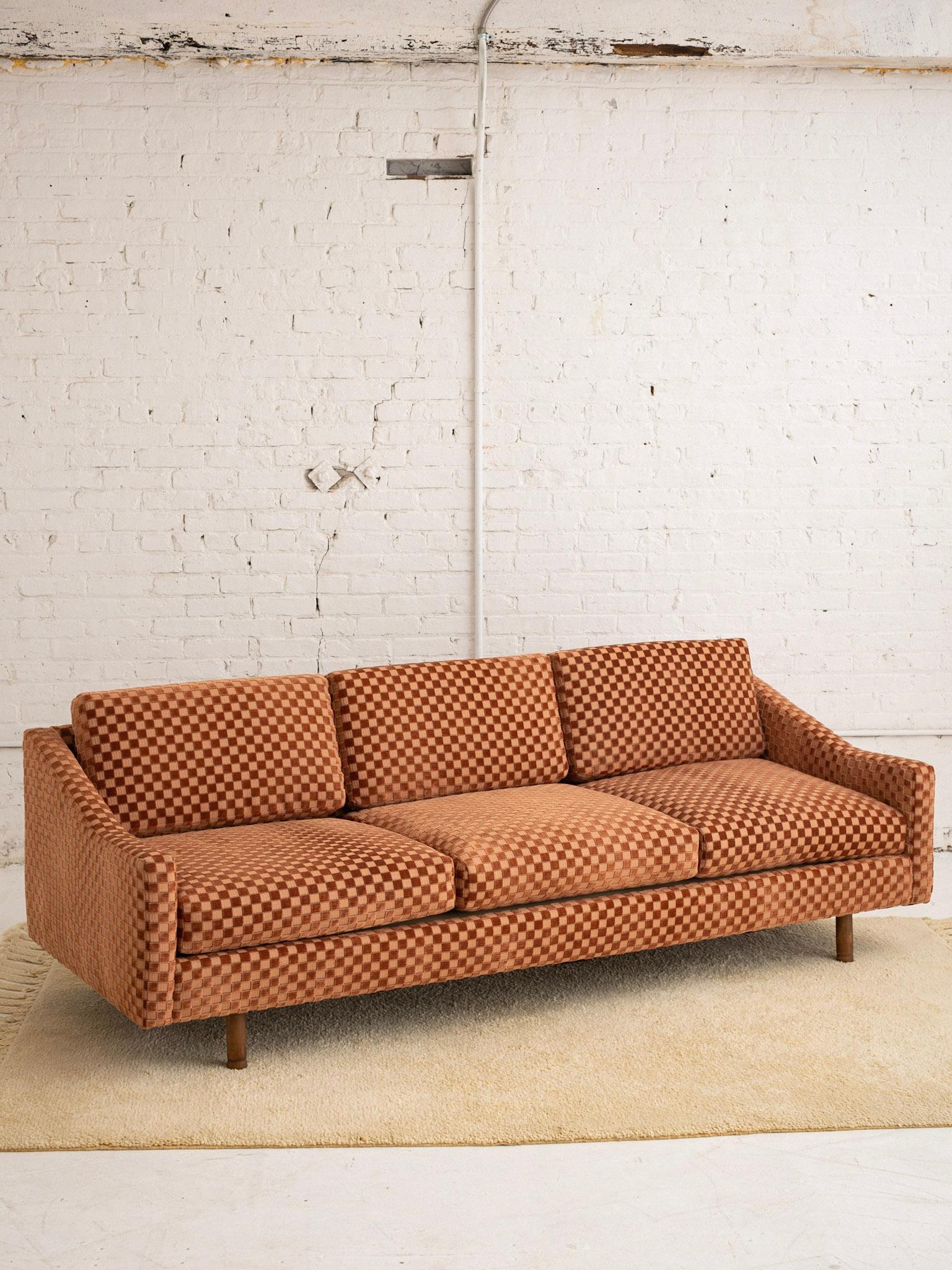 A mid century modern sofa by Selig. Classic streamlined silhouette. Newly upholstered in a checkered velvet. Fabric appears a soft burgundy color but reveals threads of olive green upon close inspection. New foam cushions.