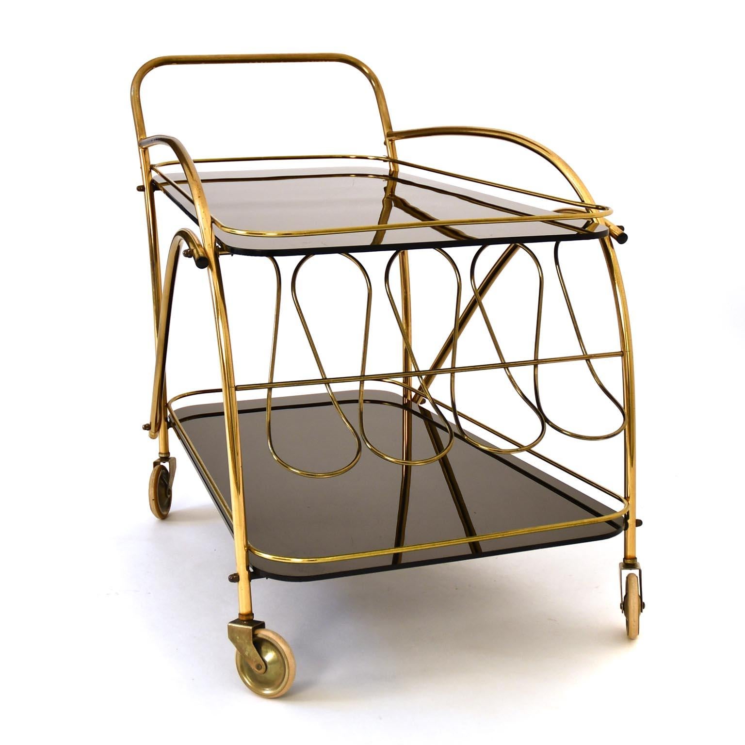 The serving trolley captivates with its shape, which conveys both lightness and elegance. The bottle holders made of dynamic brass loops give the serving trolleys a very special touch. The black glasses are in original condition, slightly scratched.