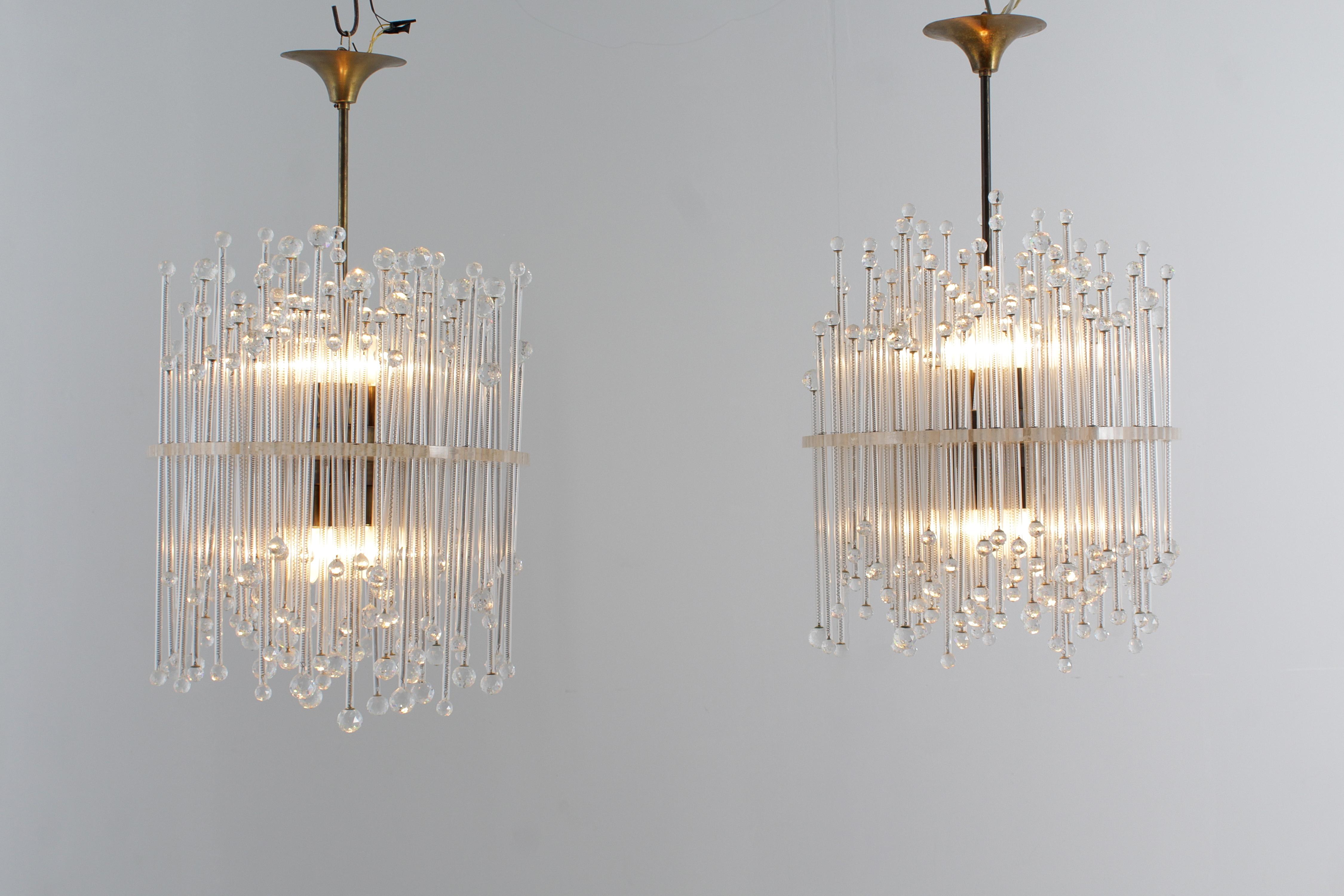 Stunning and impactful pair of glass chandeliers, Italian production from the 1960s.
The chandeliers have a central plexiglass disc with holes that contain transparent glass tubes of different heights, inside which metal wire springs hold two