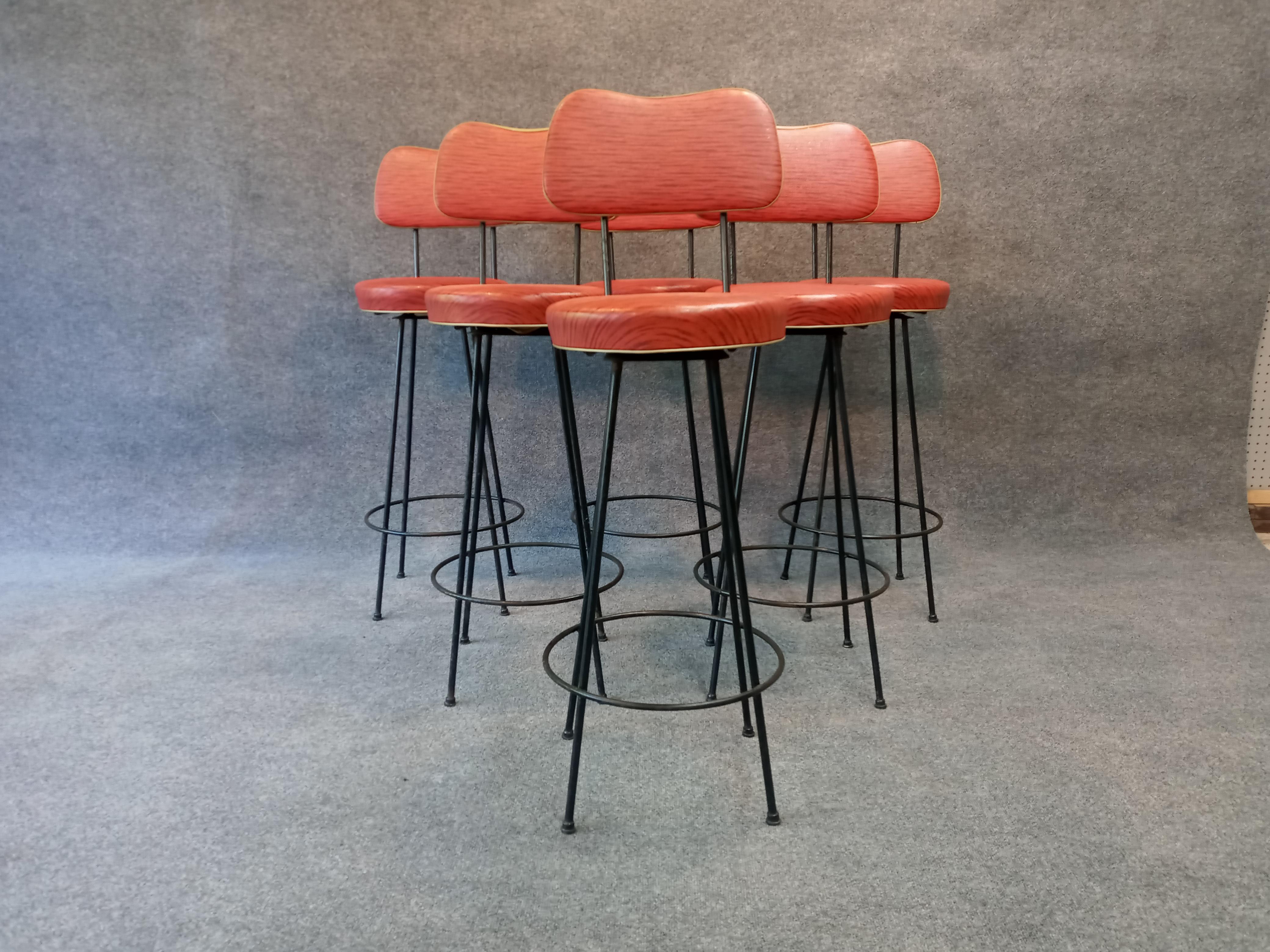 An amazing time capsule clean original set of swivel barstools retaining original finishes. Each retains original enamel on iron bases, black plastic feet, original red with black striping vinyl upholstery with gold piping.