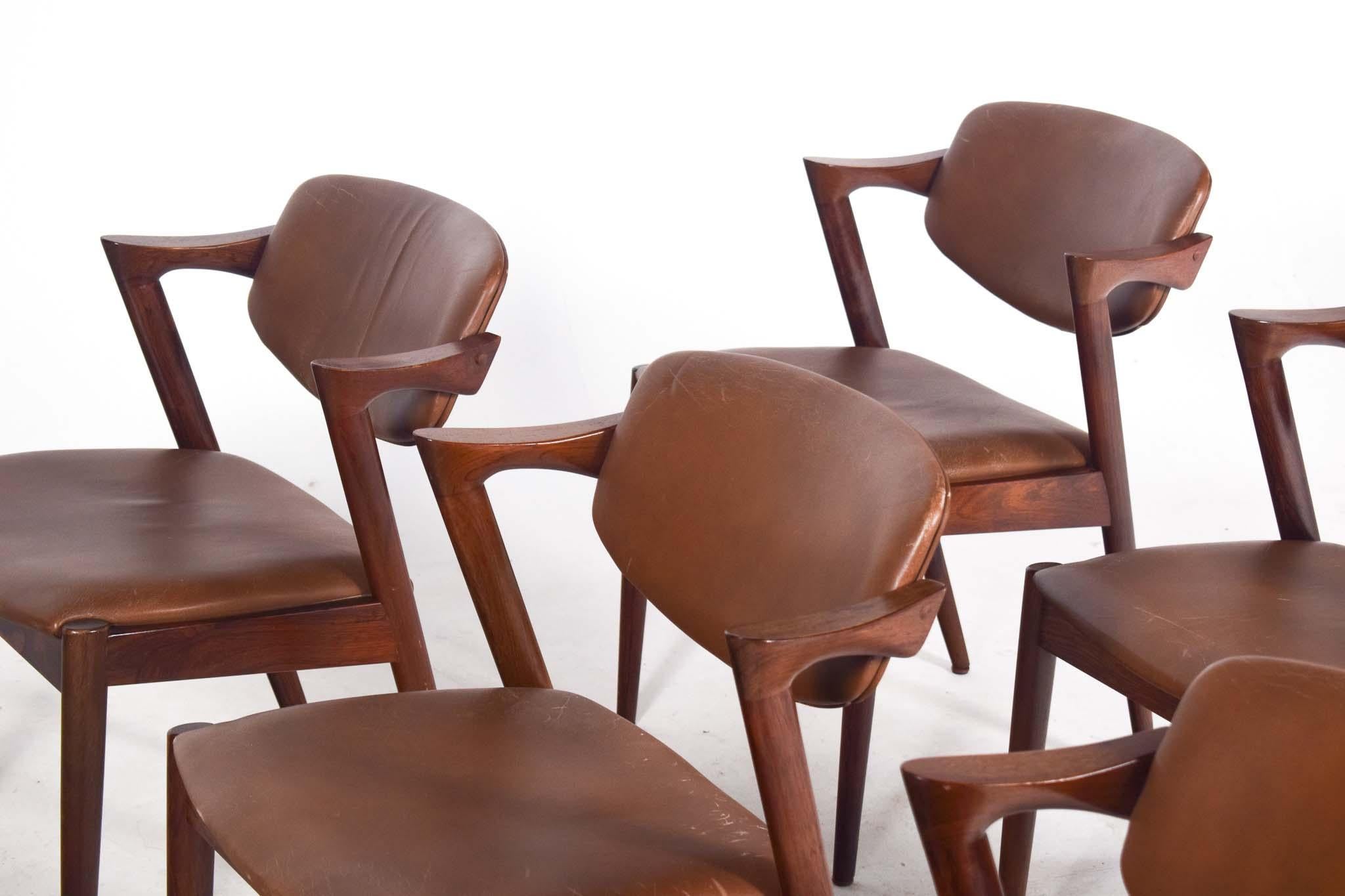 This set of 6 dining chairs, model 42, is a mid-century modern masterpiece designed by renowned Danish designer Kai Kristiansen in 1963. Crafted from rich rosewood, these chairs are celebrated for their impeccable craftsmanship and timeless
