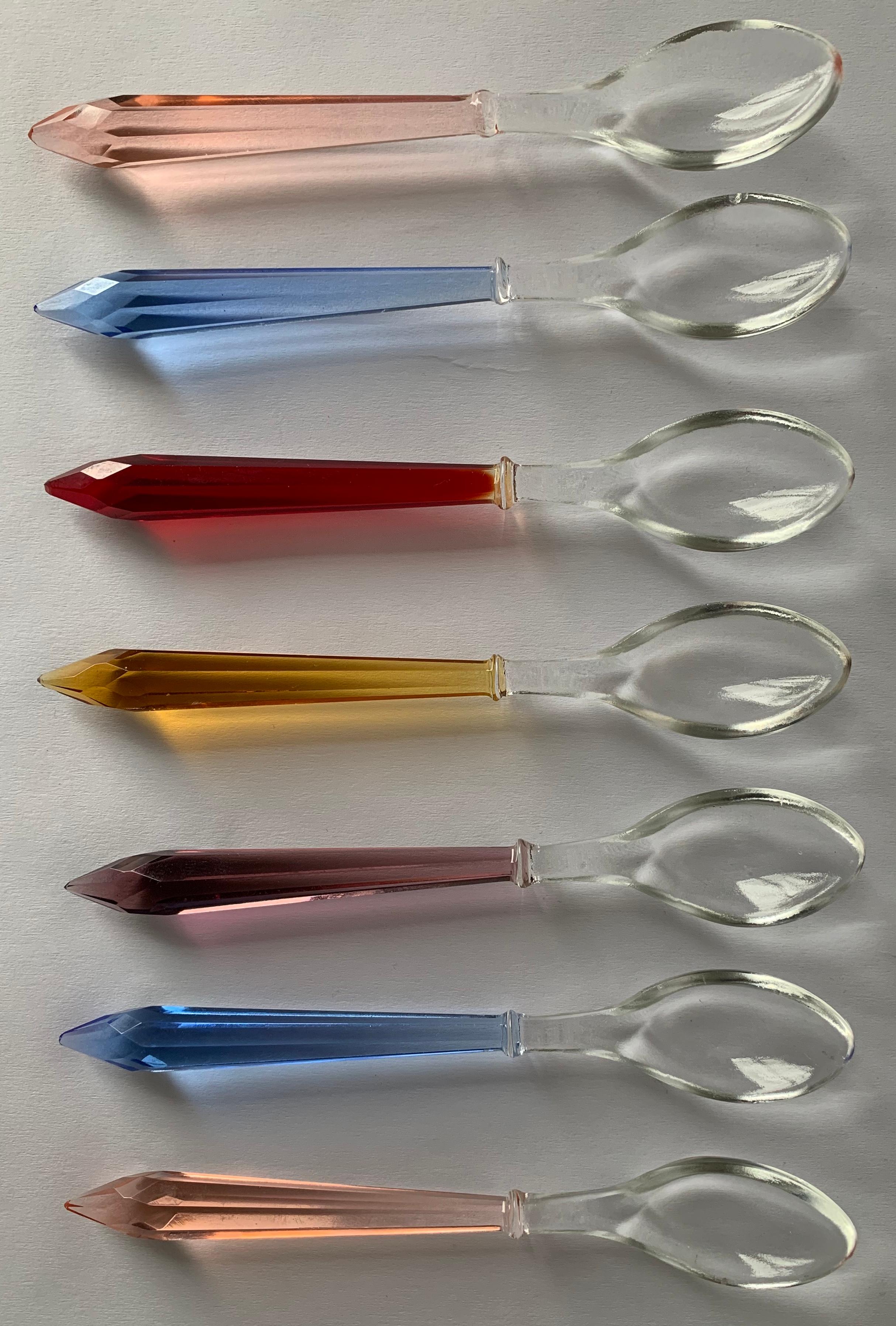 Set of 7 midcentury small glass serving or demitasse spoons. Each spoon has a colored cut glass prism handle in red, blue, orange, purple and pink. No makers mark or signature.