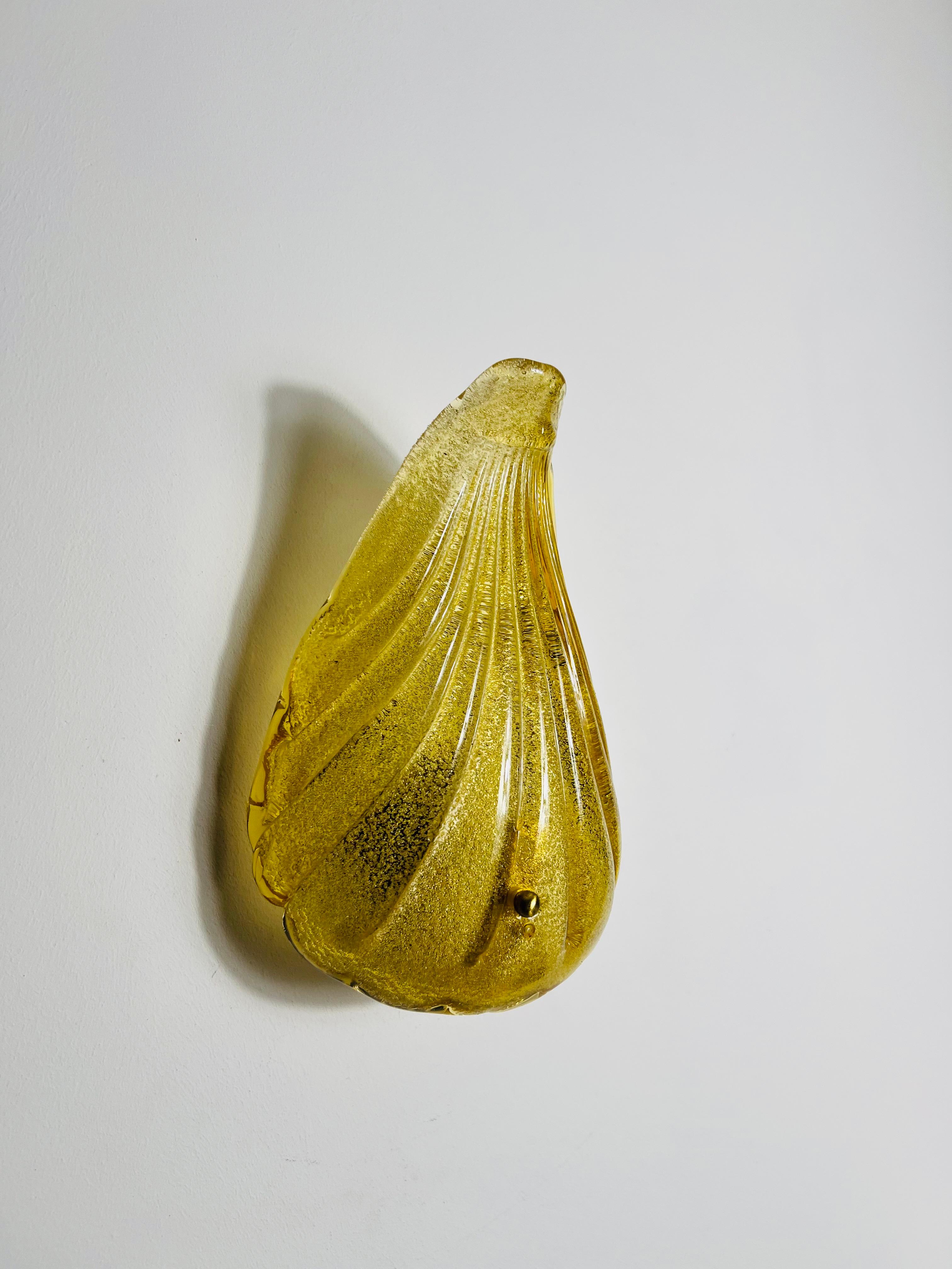 This exquisite wall lamp from the 1960s is a true testament to Italian craftsmanship, featuring hand-blown Murano glass in a refined shell shape. The structured glass showcases a delicate greenish-yellow hue that exudes warmth and elegance. Its