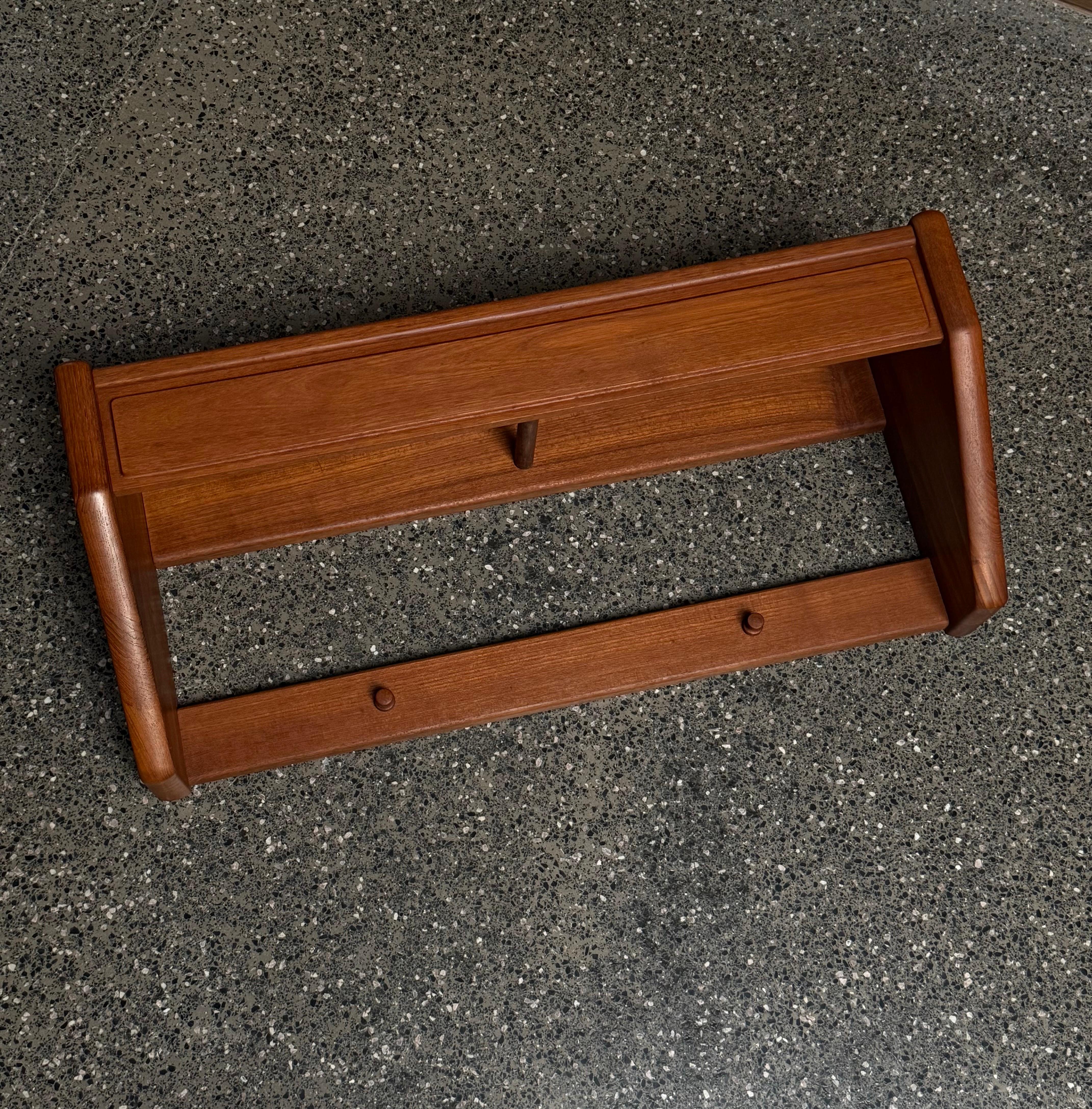Mid-century teak wall mounted shelves. We have two available and price is per shelf. Designed and manufactured by Dyrlund, Denmark circa 1960s. A multipurpose shelf that has pegs to serve as a coat rack and a teak shelf atop for keys and other