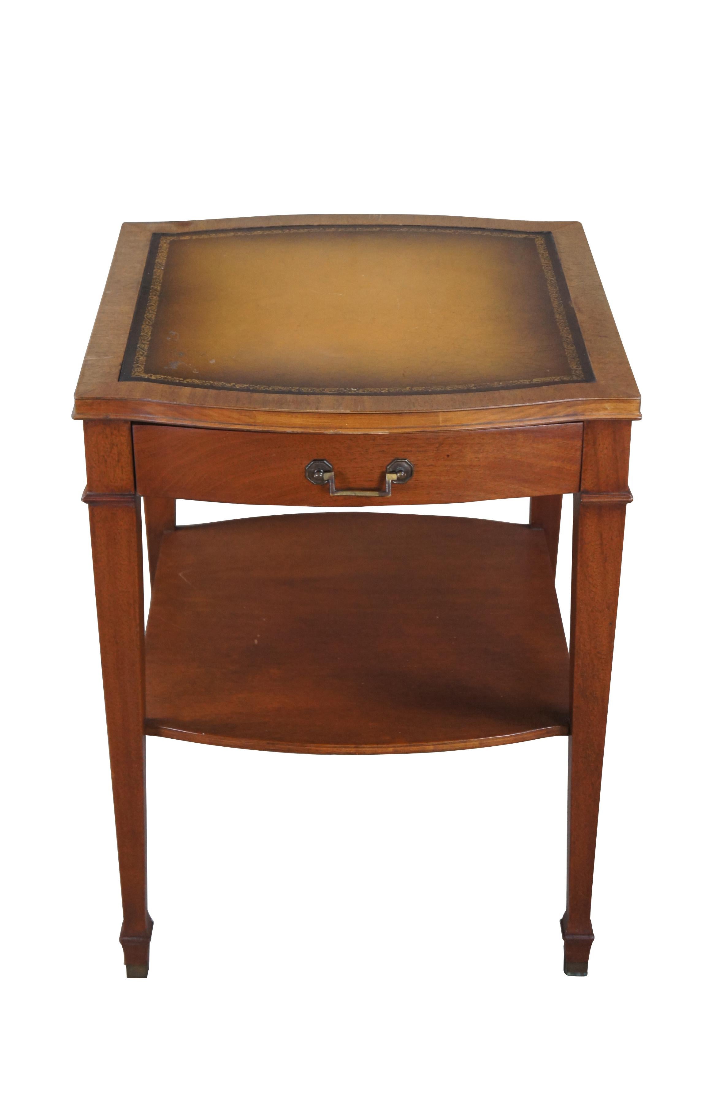 Mid 20th Century mahogany side or end table.  Features a traditional Sheraton style form with a serpentine tooled leather top. The table has one drawer with bale hardware and a lower drawer.  Supported by square tapered legs with spade feet.  The