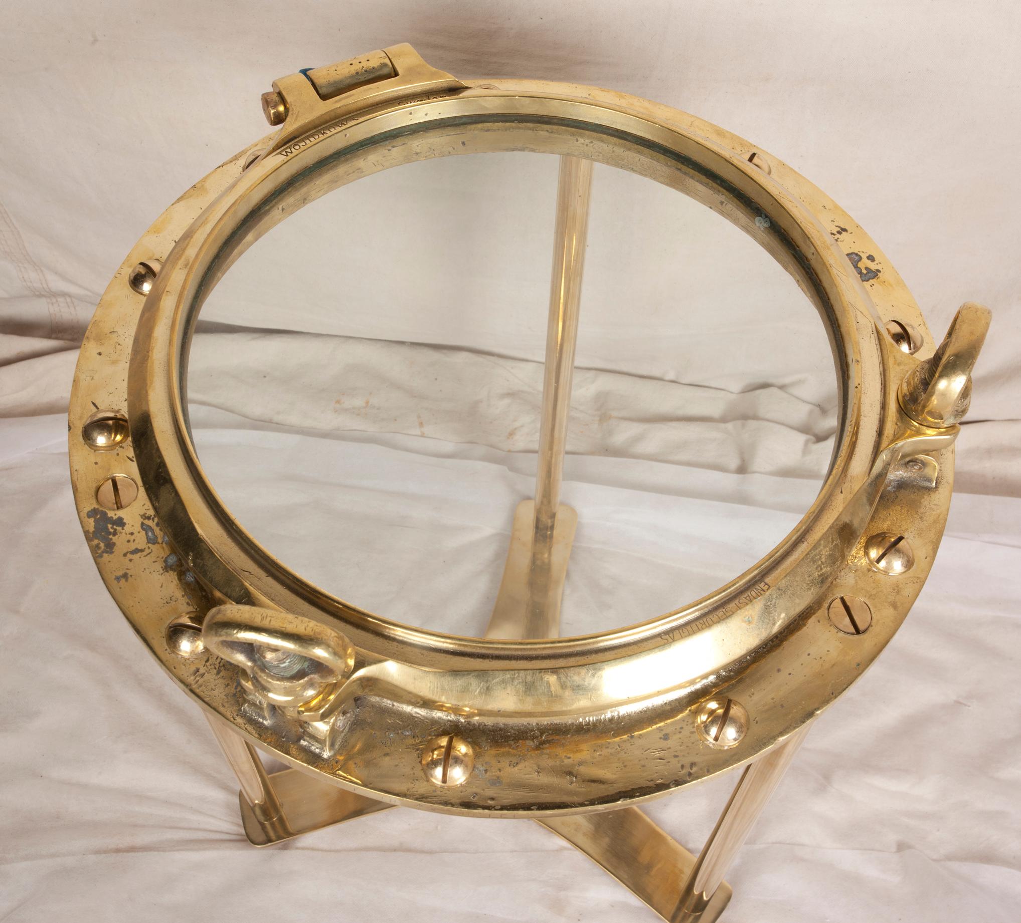 Solid brass working nautical porthole window from a decommissioned ship with great patina. This has been polished, the rivets put back in and the table base designed by Deborah Lockhart Phillips is able to disassemble if needed. Use as a side or
