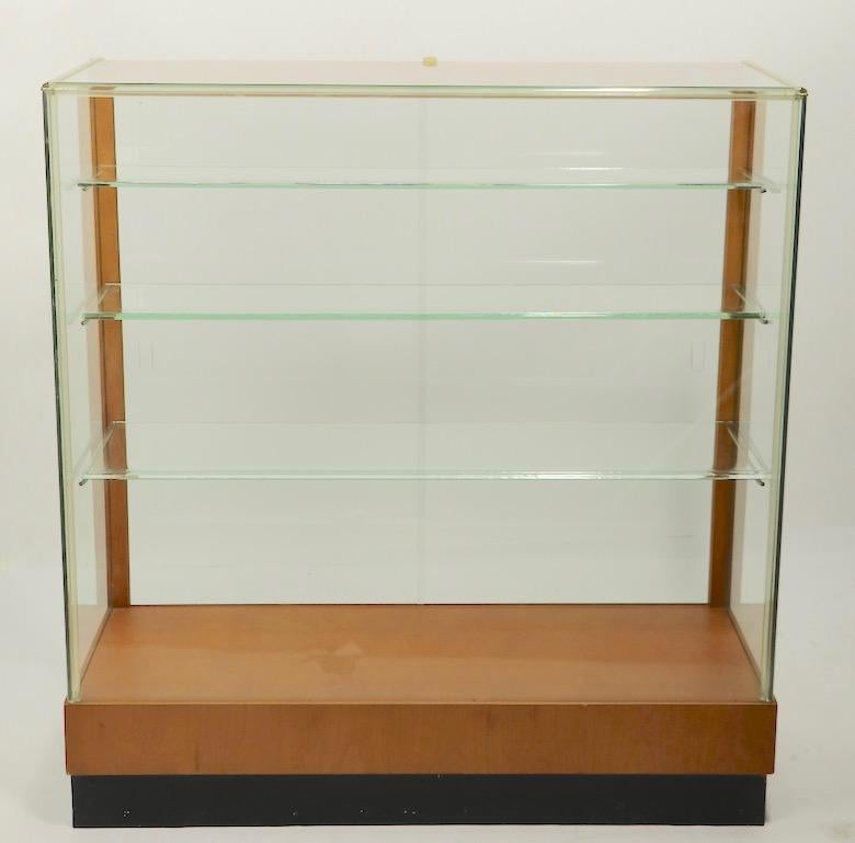 Nice clean midcentury showcase having two sliding doors, glass sides and front, Lucite trim with three graduated glass shelves. The glass case has a maple frame and blonde veneer bottom, on black plinth base - manufactured by Waddell. Originally