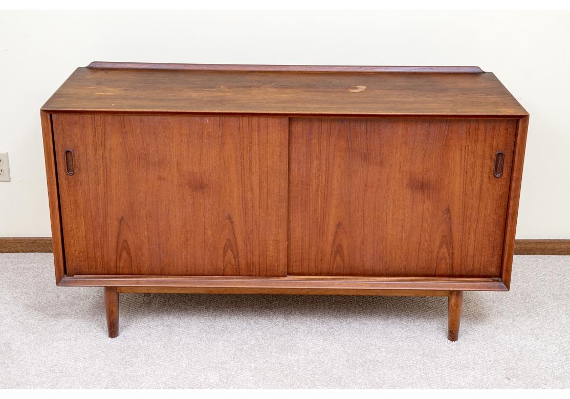 Credenza classica in teak della metà del secolo scorso con ante scorrevoli, risalente agli anni '50/'60. La credenza ha dimensioni ridotte ed è utile per molte applicazioni. Le ante scorrevoli si aprono per rivelare un interno in faggio con quattro